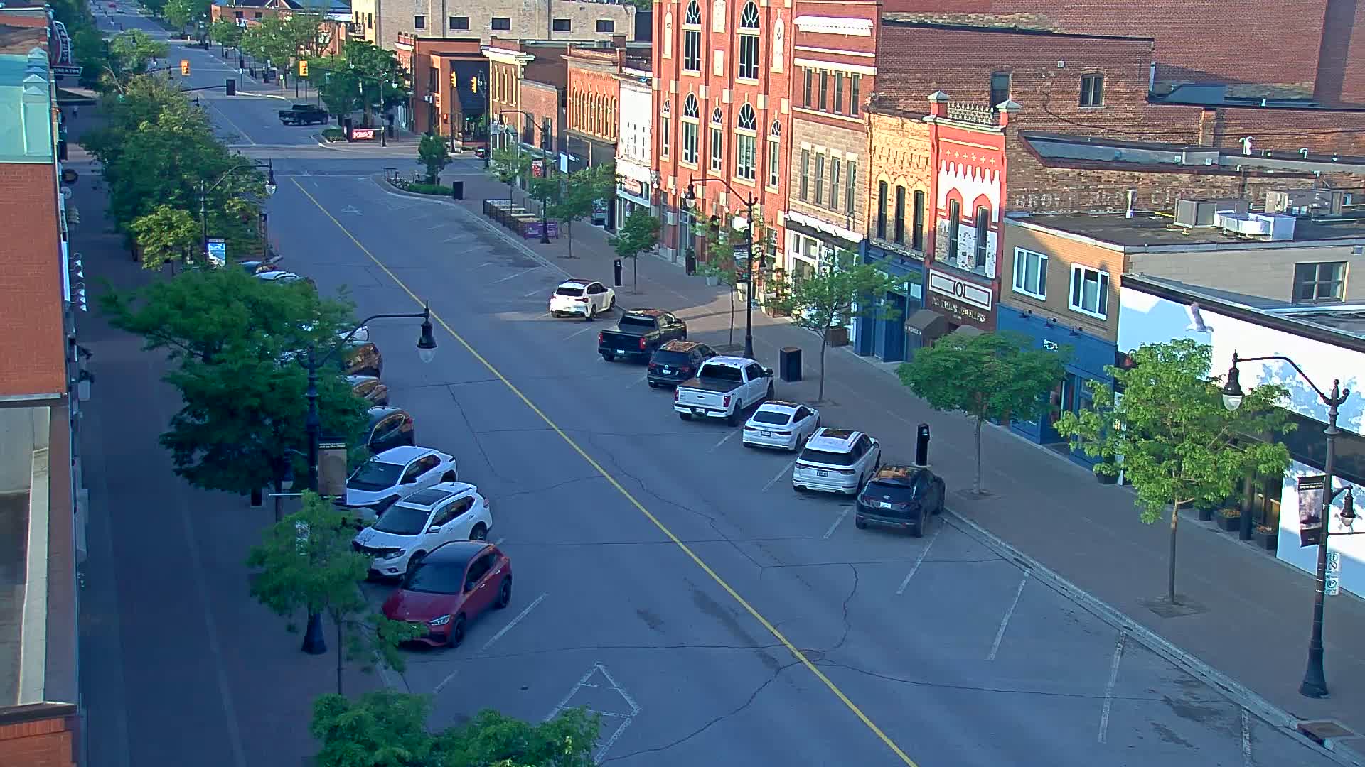 A street lined with parked cars and brick buildings on a partly sunny day.