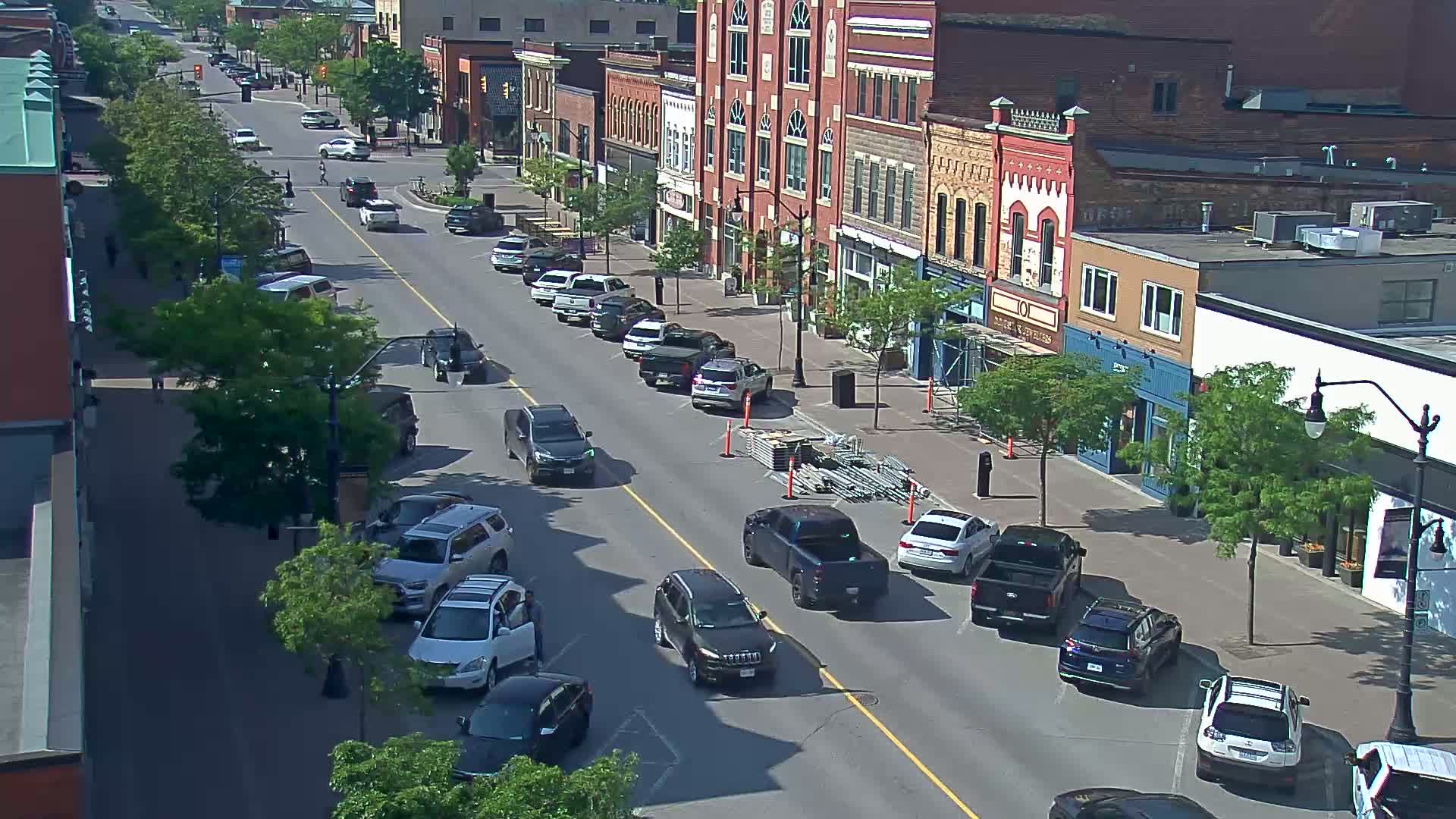 A sunny day reveals a city street lined with parked cars and brick buildings, with construction scaffolding visible near the center.