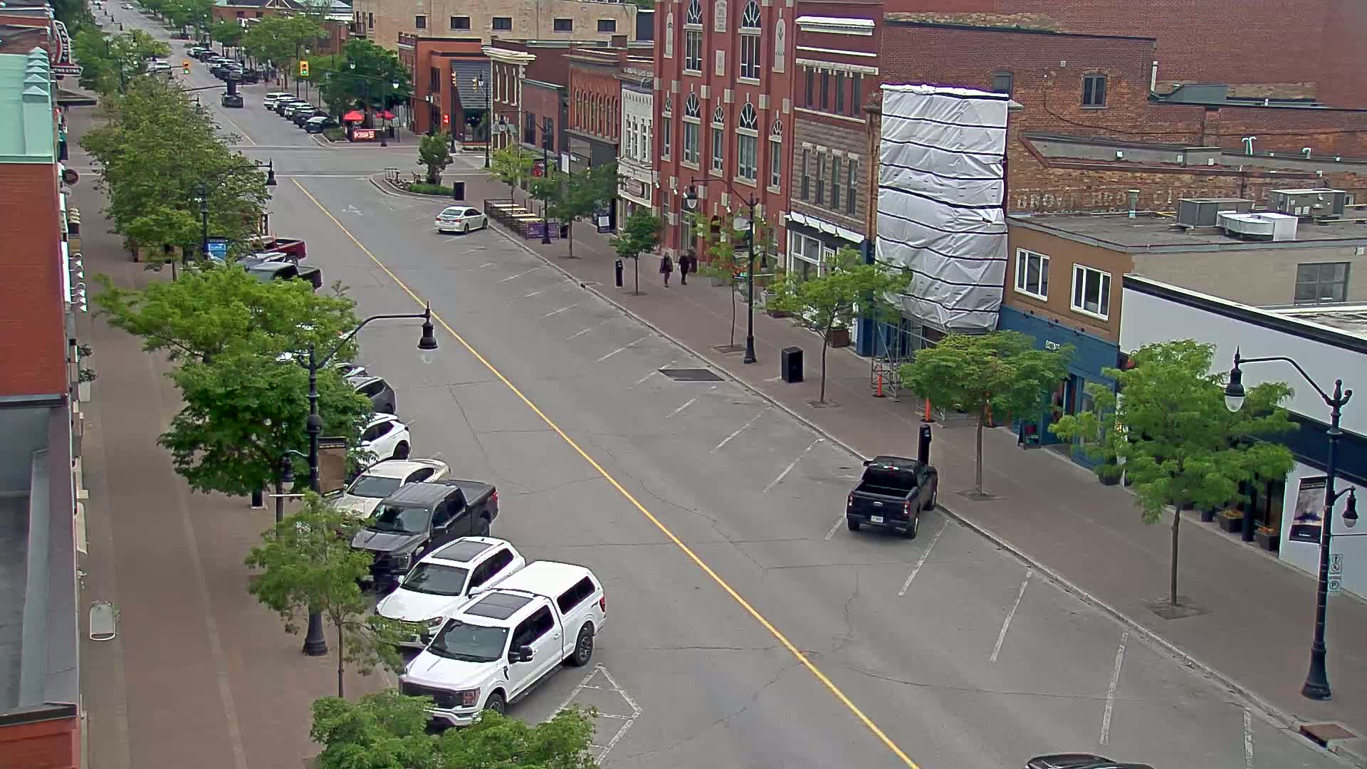 A mostly empty street lined with parked cars and brick buildings on a cloudy day.