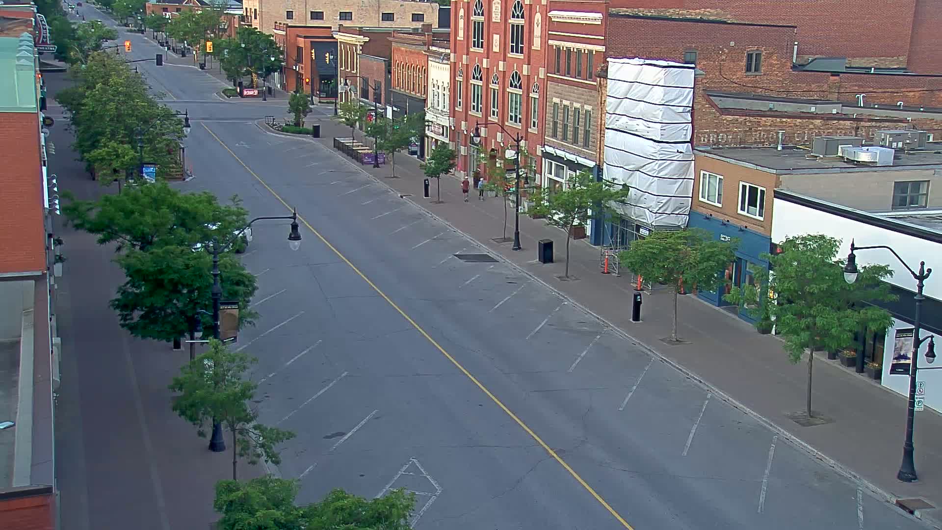 A mostly empty street lined with brick buildings and green trees on a sunny day.