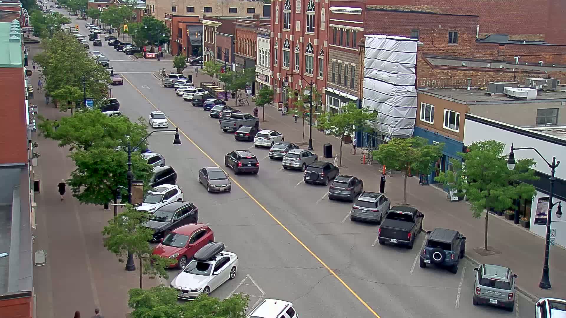 A city street lined with parked cars on both sides, under a partly cloudy sky.