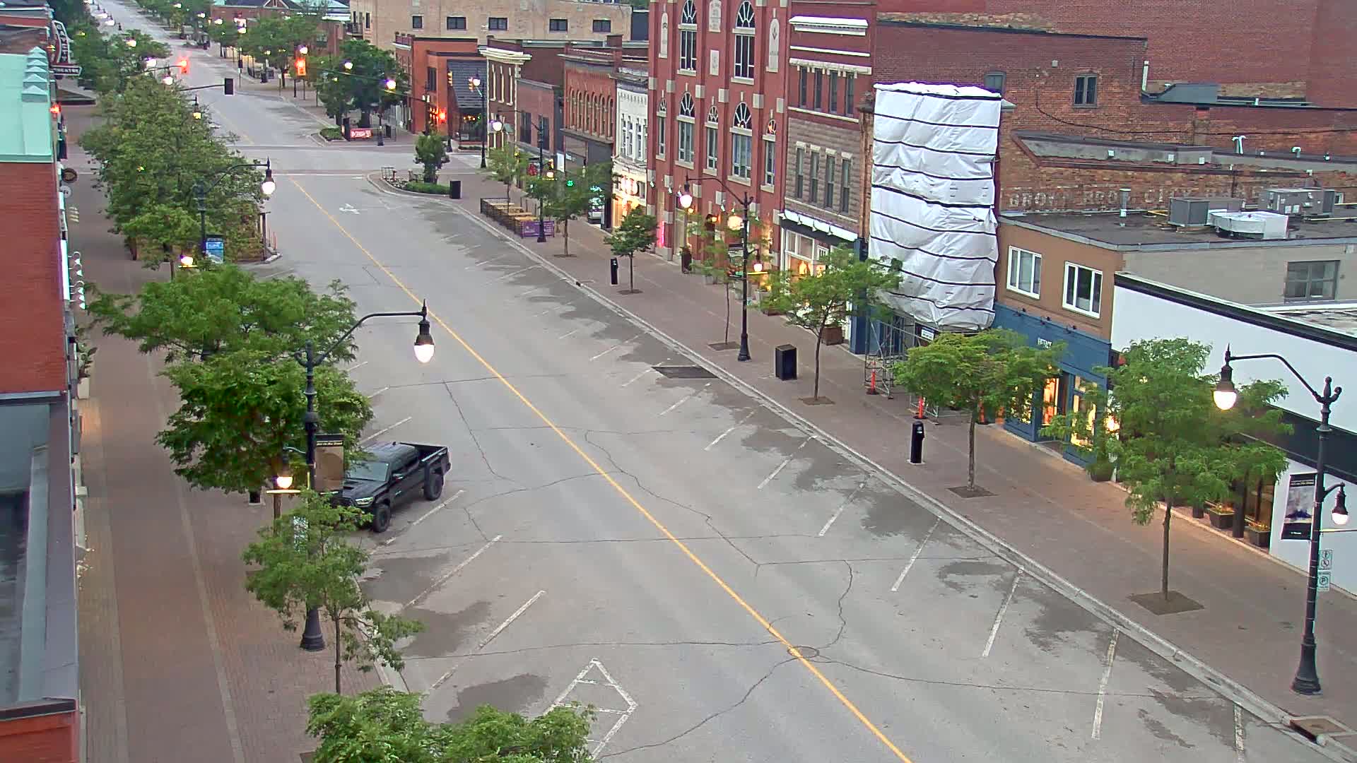 A mostly empty street lined with brick buildings and trees on a partly cloudy day.