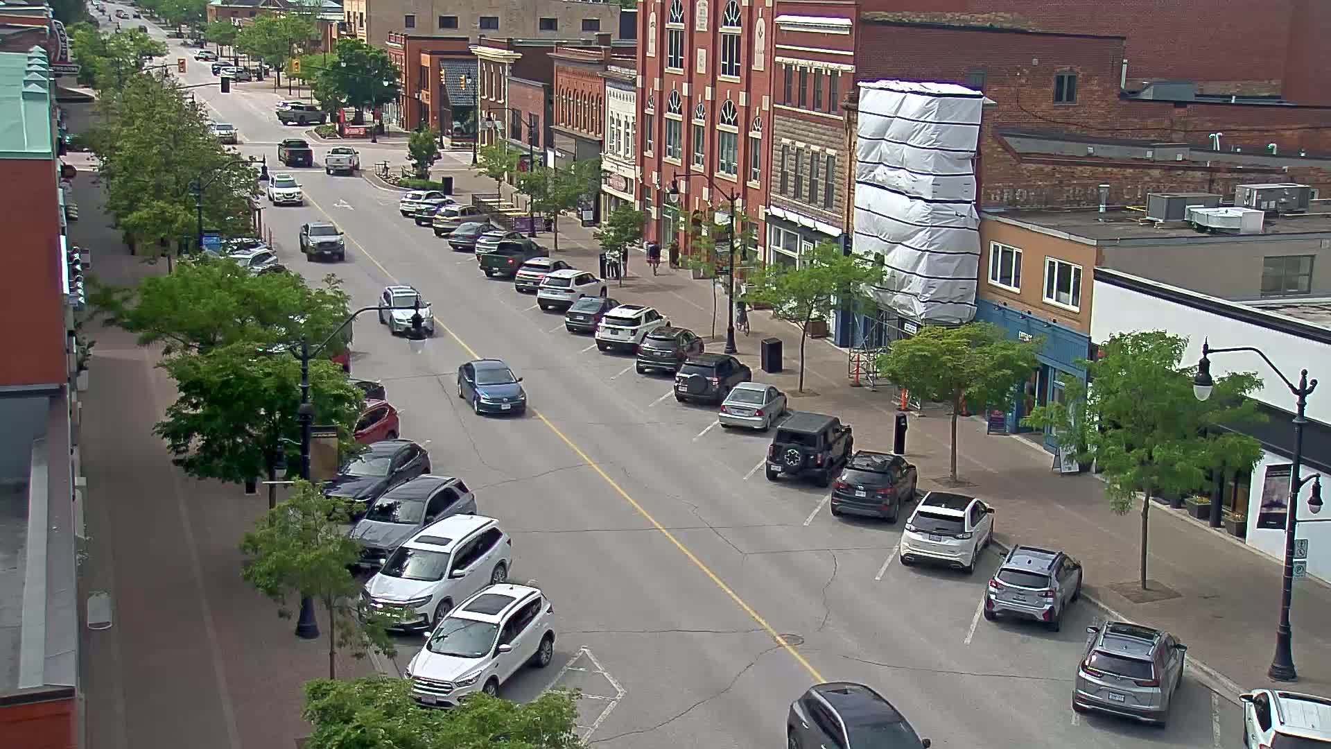 A sunny day reveals a street lined with parked cars and brick buildings, some of which are under construction.