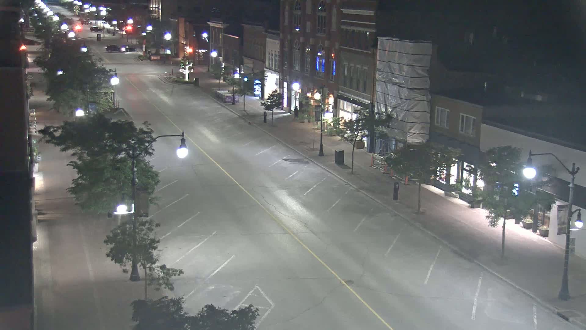 A mostly empty, illuminated street at night lined with buildings and trees.