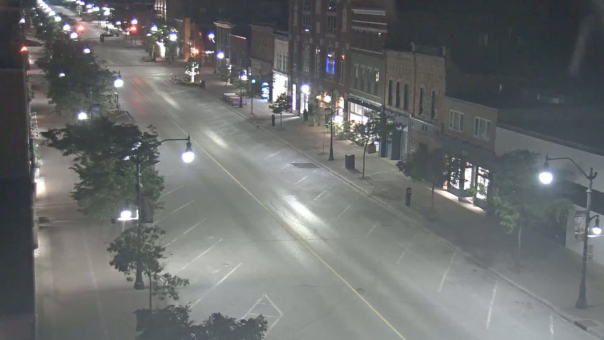 A mostly empty street at night, lined with two-story buildings and streetlights, under clear skies.