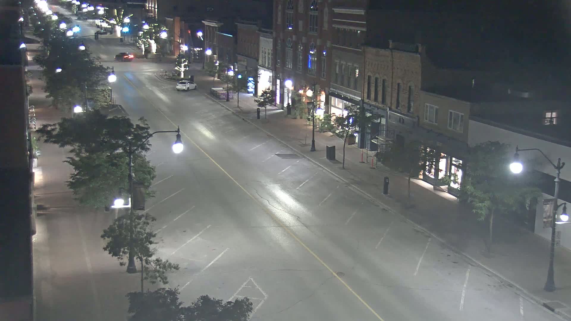A mostly empty street at night, lined with two-story buildings and streetlights, under clear skies.