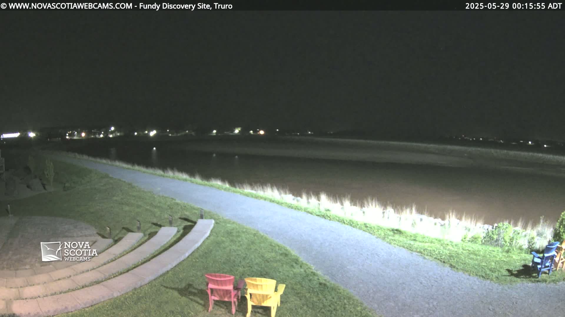A nighttime view of a paved path leading to a body of water, with an amphitheater and colorful chairs in the foreground.