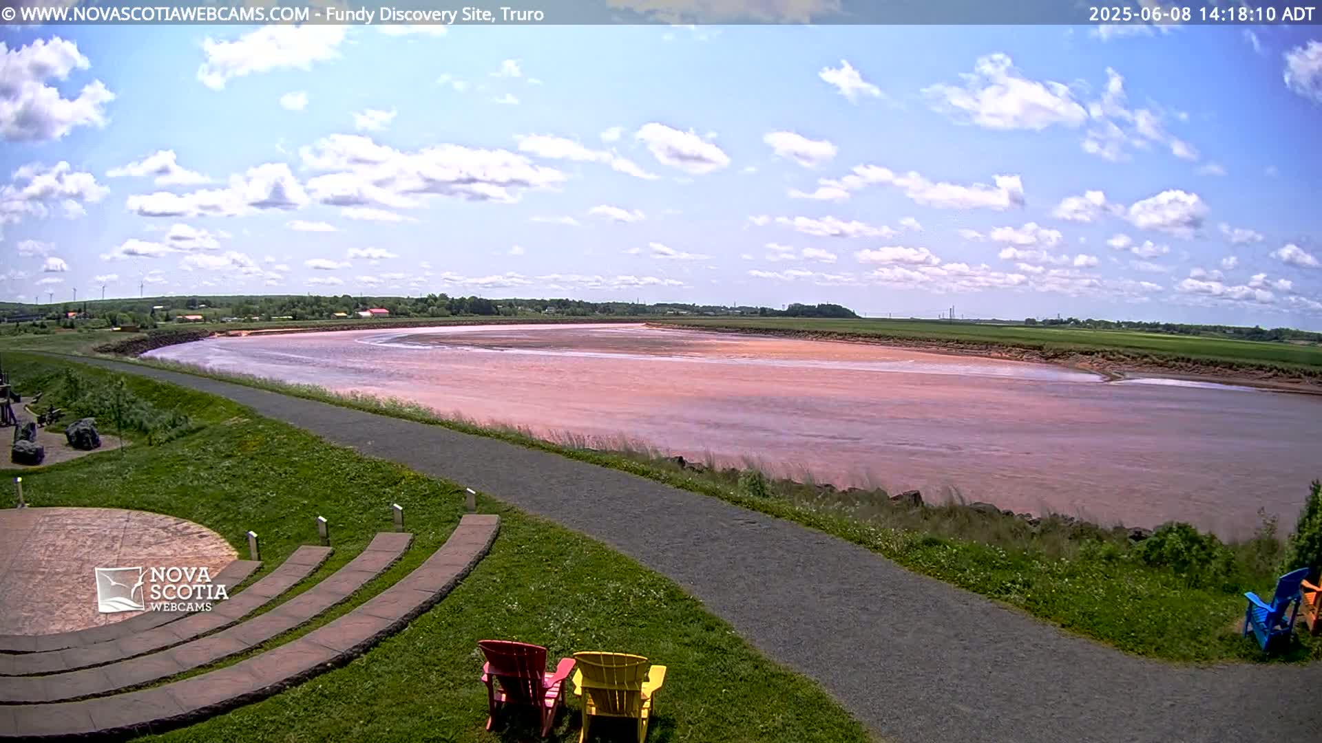 A wide, pinkish-red river flows through a grassy landscape under a partly cloudy sky.