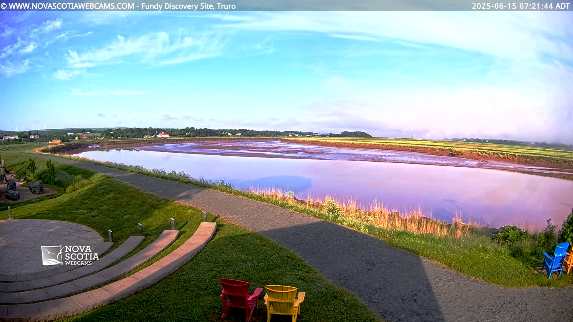 A calm river reflects a pastel sunrise sky, with a paved path and amphitheater-like seating area in the foreground.