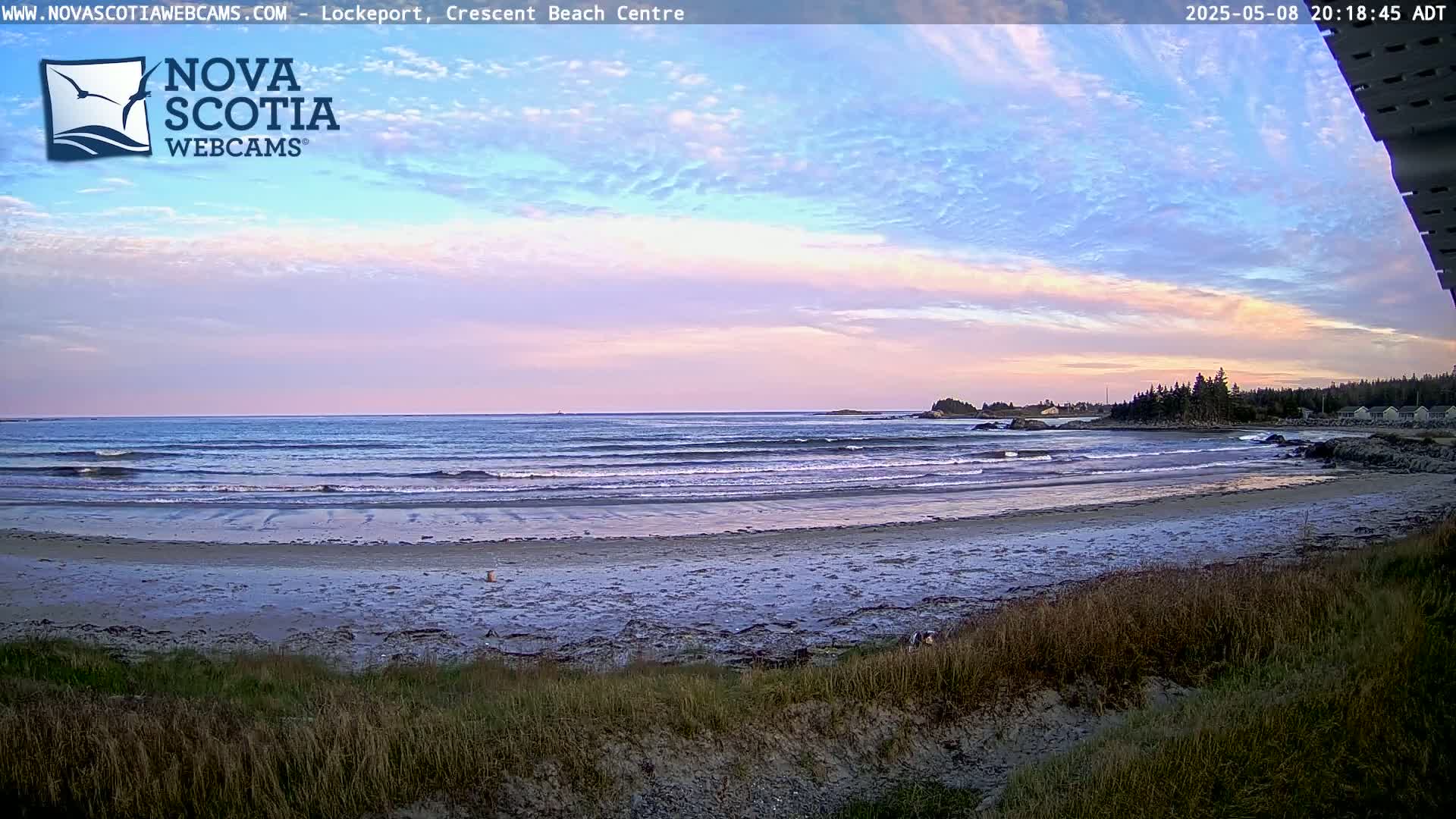 A sandy beach with gentle waves laps the shore under a pastel sunset sky.