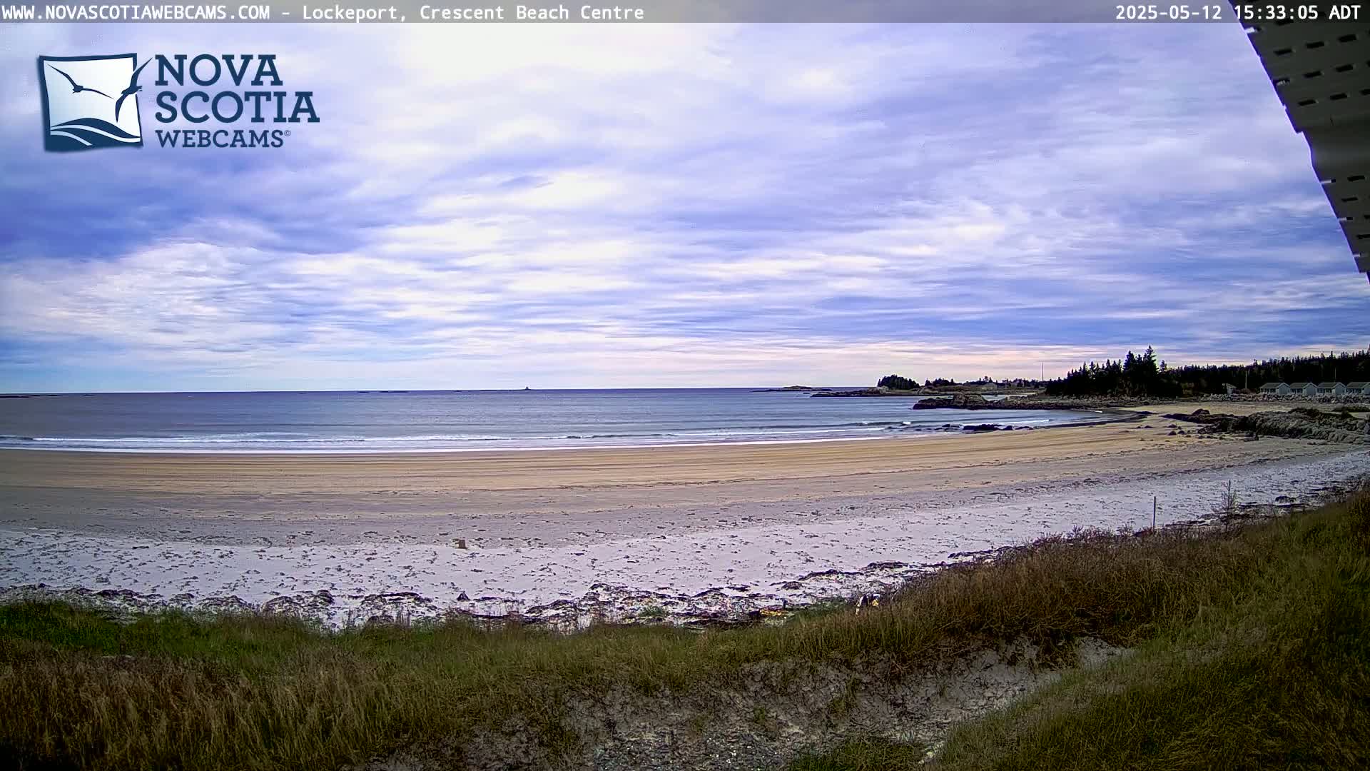 A sandy beach stretches towards a calm ocean under a partly cloudy sky.