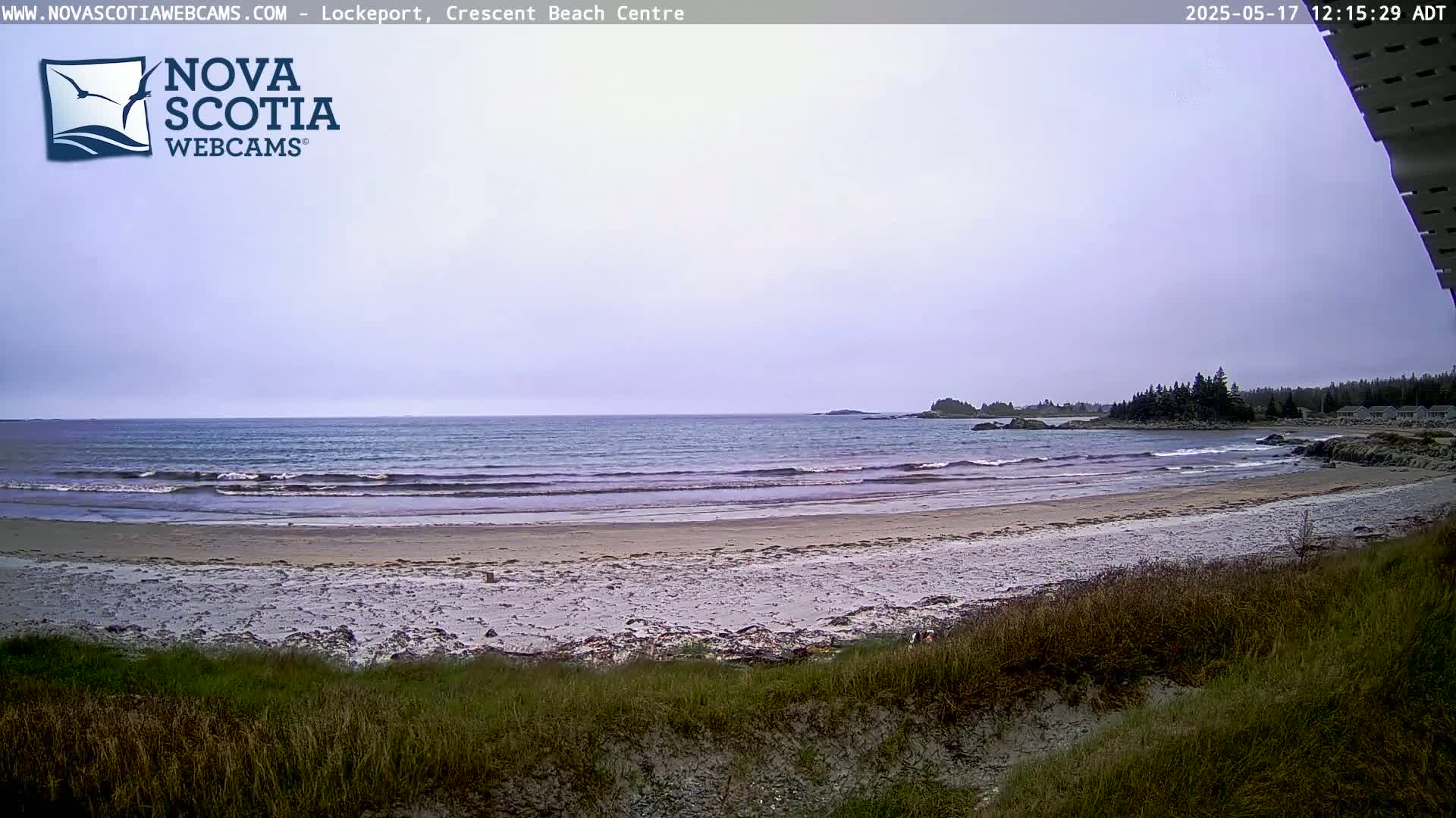 A sandy beach with gentle waves rolls onto the shore under an overcast sky.