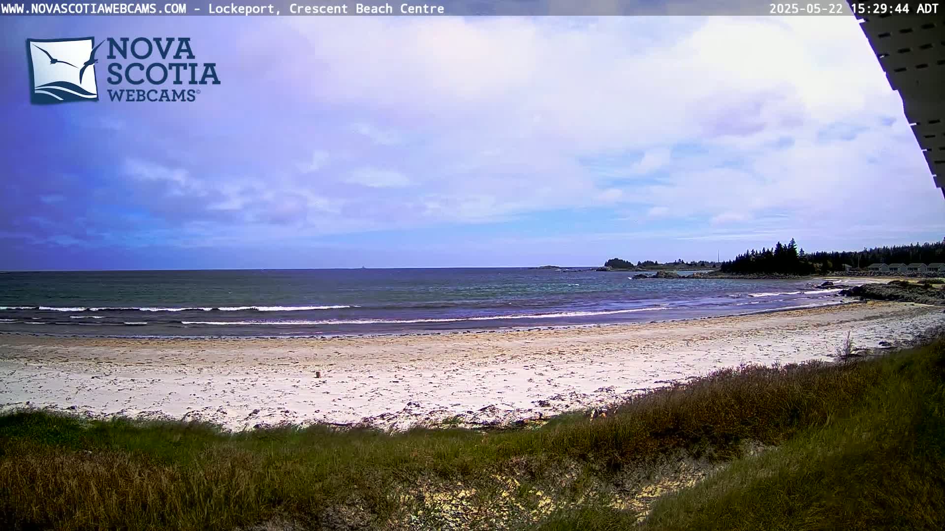 A sandy beach with gentle waves laps the shore under a partly cloudy sky.