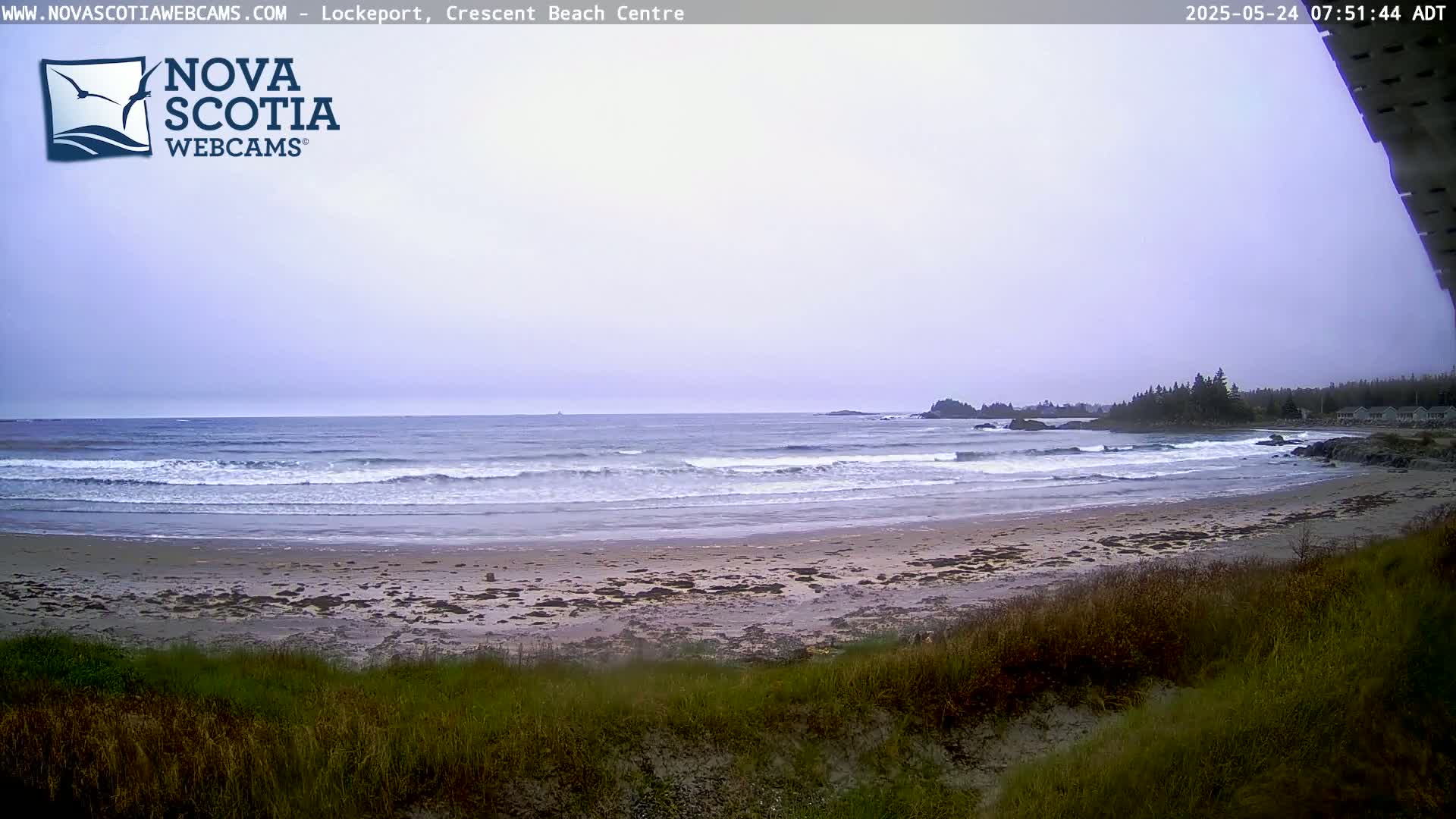 A sandy beach with small waves rolls onto the shore under an overcast sky.