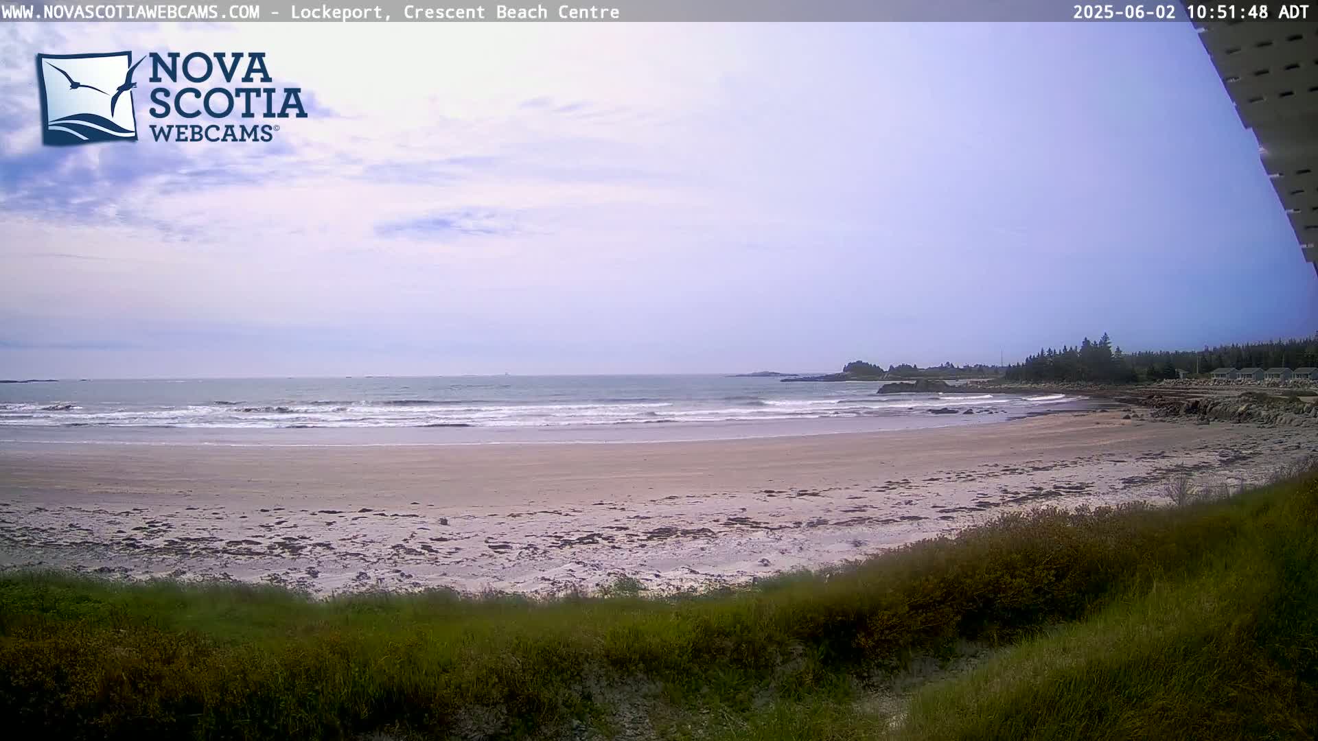 A sandy beach with small waves gently lapping the shore under a partly cloudy sky.