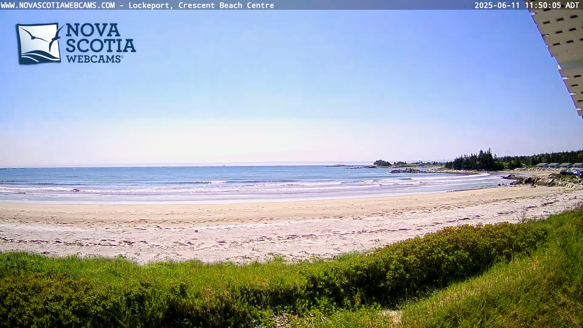 A sandy beach with small waves laps the shore under a clear blue sky.