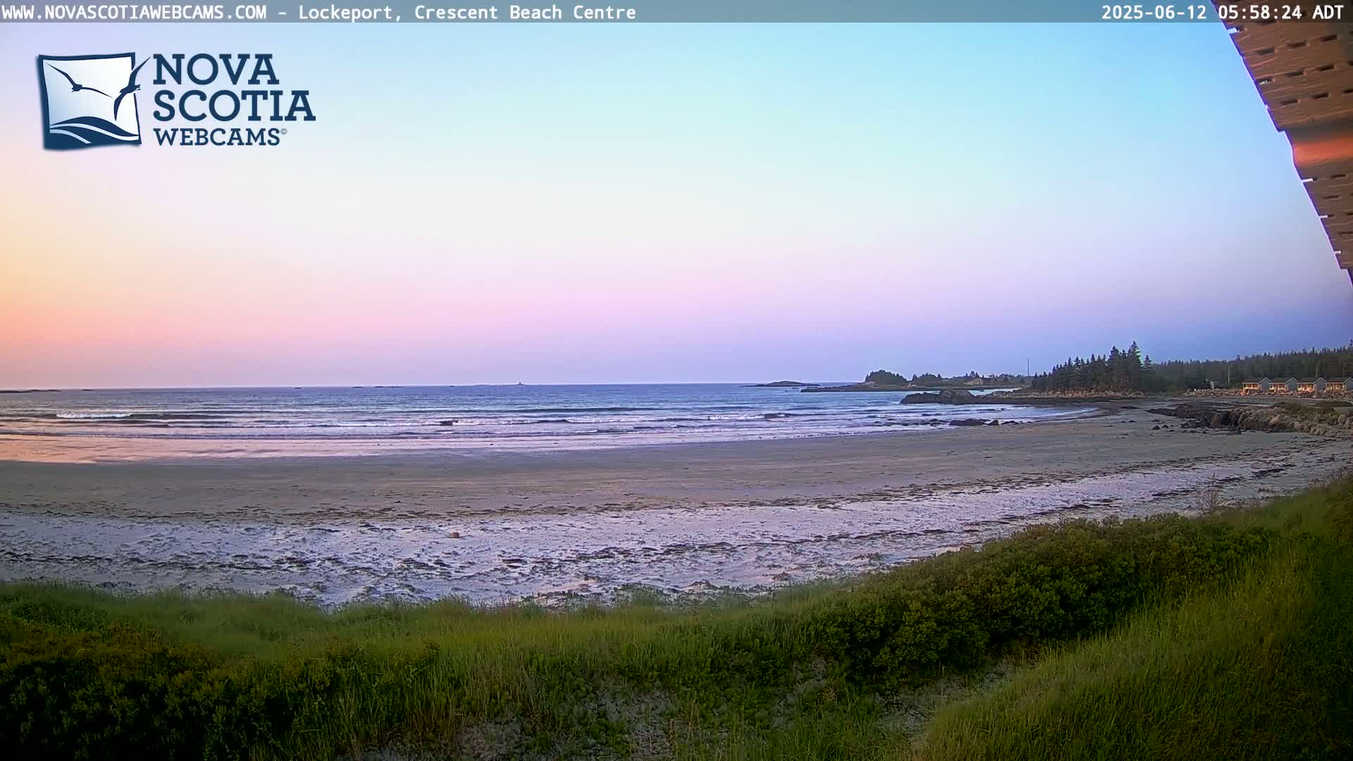A sandy beach with gentle waves under a pastel sunset sky.