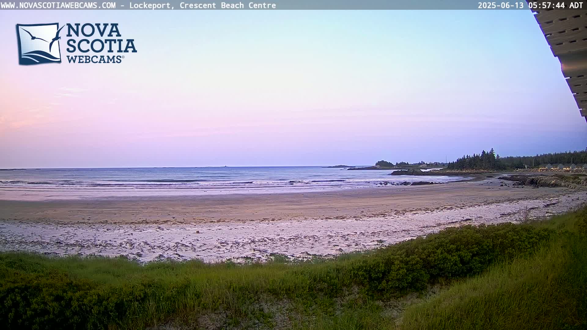 A sandy beach with gentle waves under a pale purple and pink sunset sky.