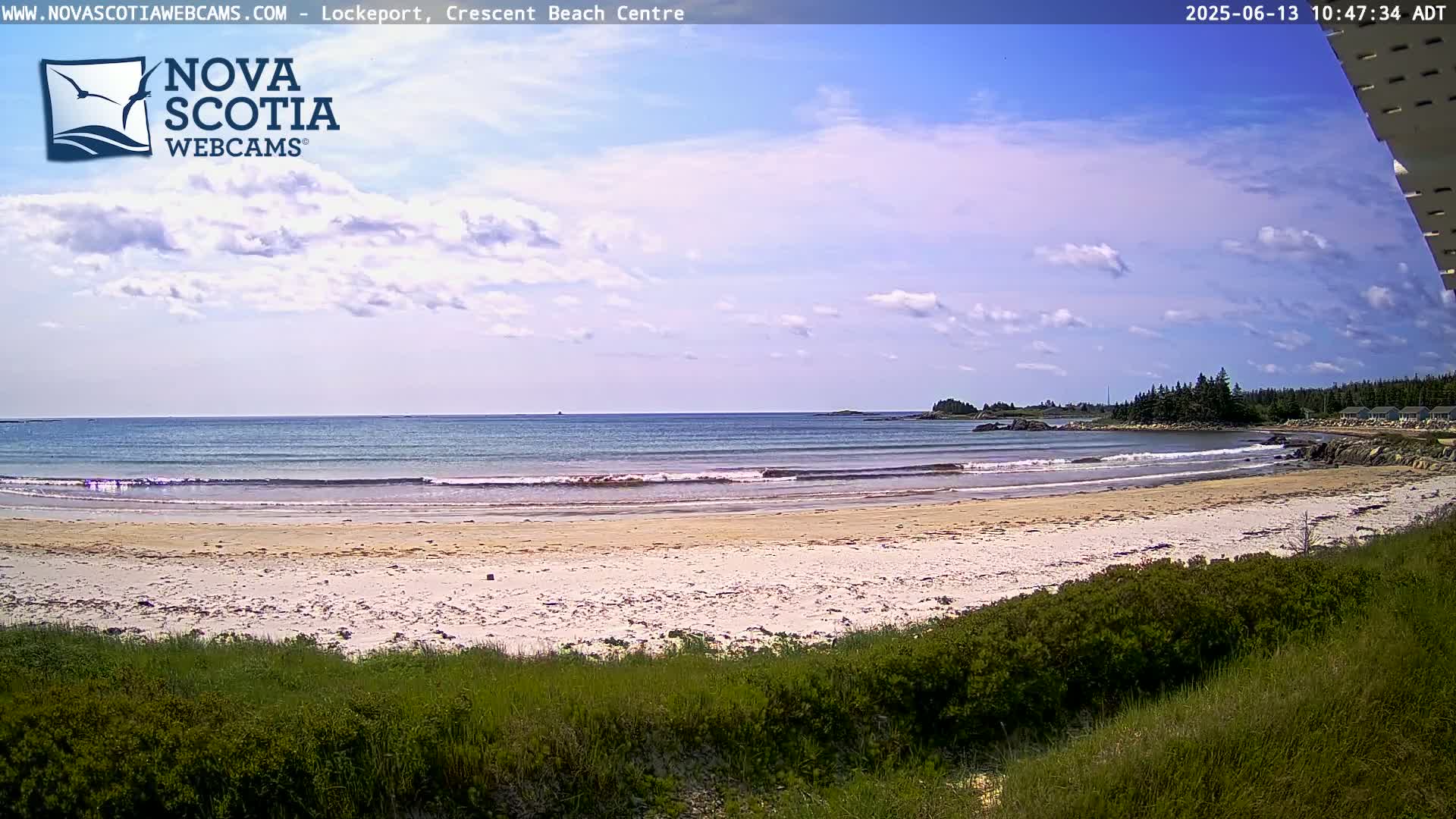A sandy beach with small waves laps the shore under a partly cloudy sky.