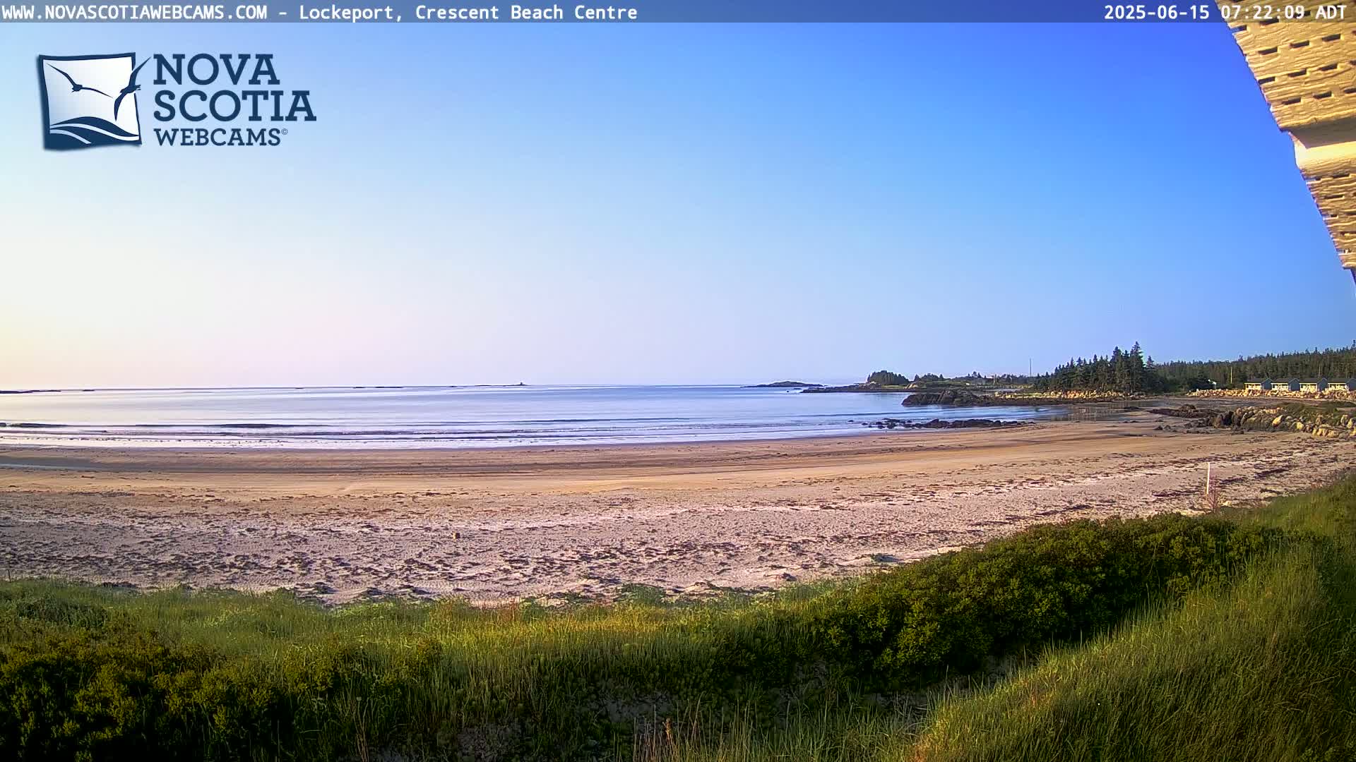 A sandy beach stretches towards a calm ocean under a clear blue sky.