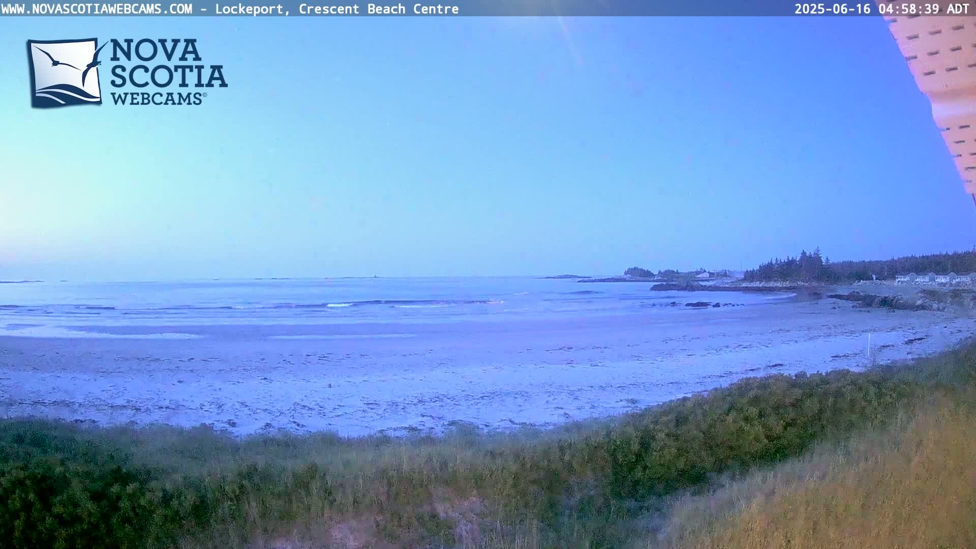 A sandy beach with calm ocean waves is visible under a clear, light blue sky at dawn.
