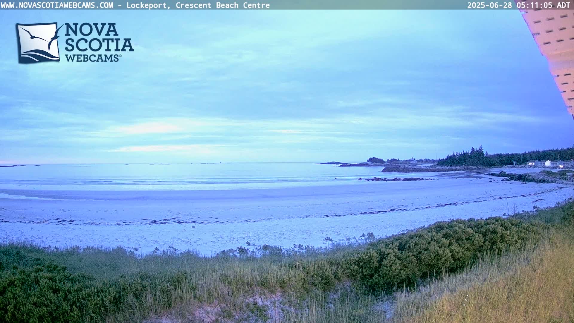 A sandy beach stretches out to a calm ocean under a pale blue, partly cloudy sky.