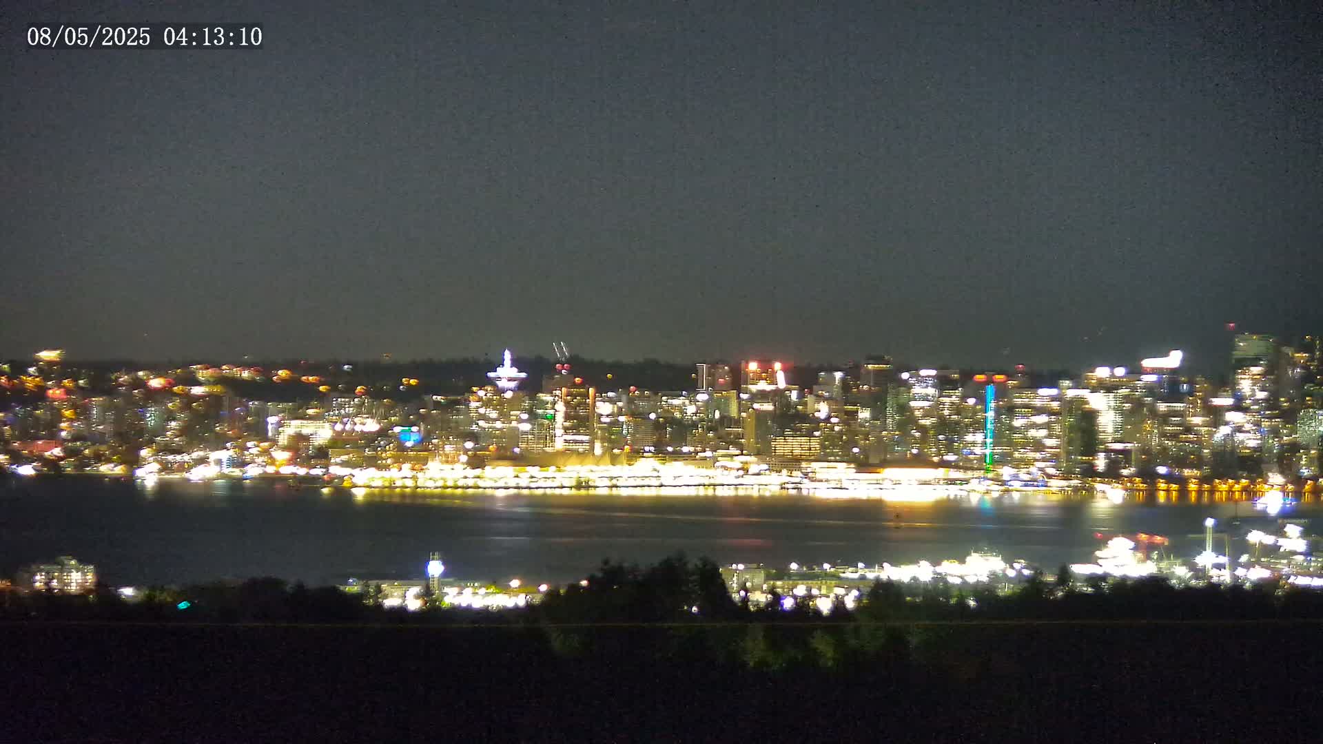 A brightly lit city skyline is visible across a dark body of water under a night sky.