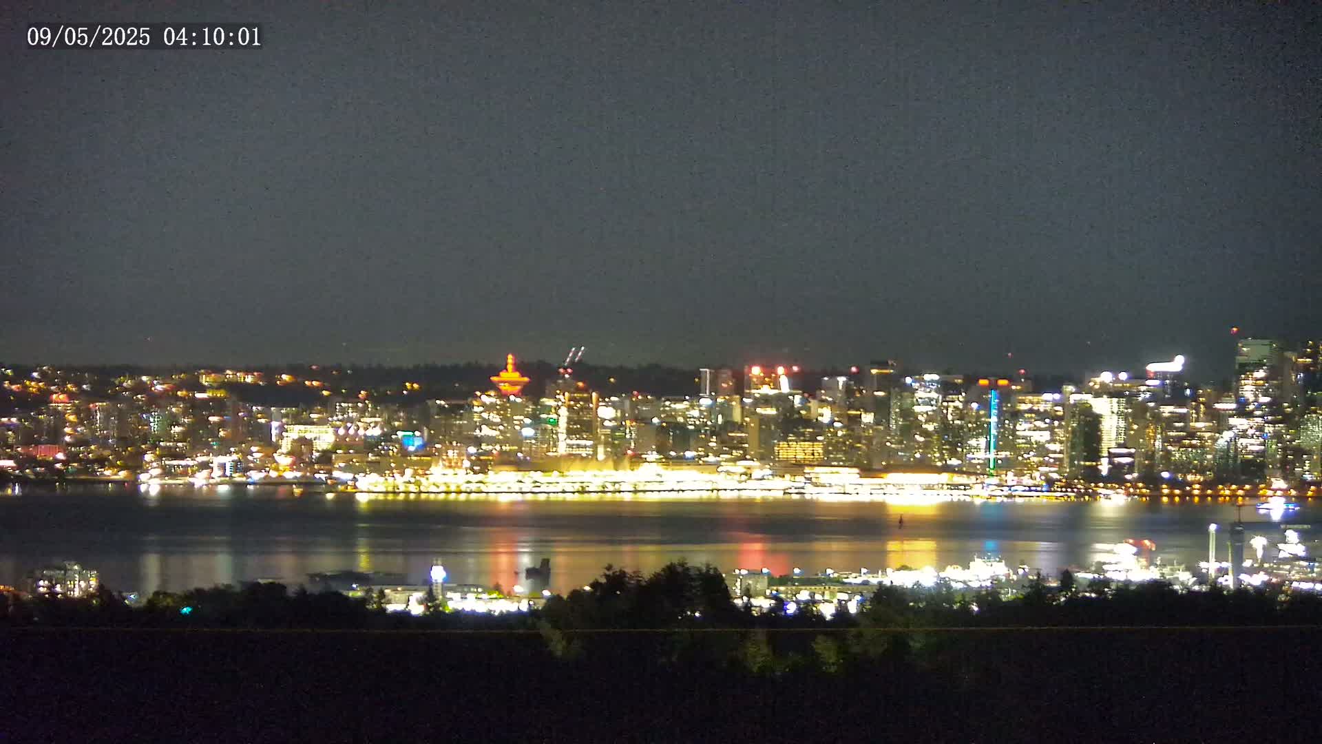 A brightly lit city skyline is seen across a dark body of water at night.
