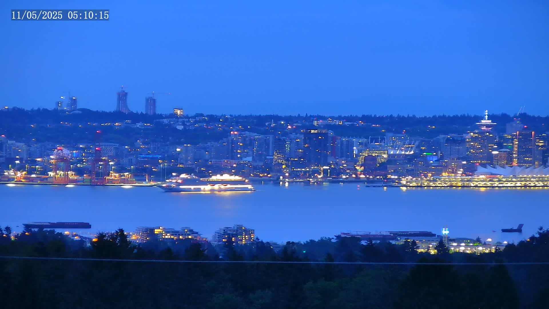 A nighttime view of a city skyline across a body of water, with a large cruise ship and many lights visible.