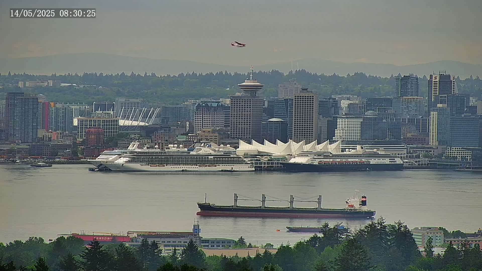 A hazy cityscape with numerous buildings, including skyscrapers and a large domed structure, is seen from afar, with a cruise ship and a cargo ship in the water in the foreground.