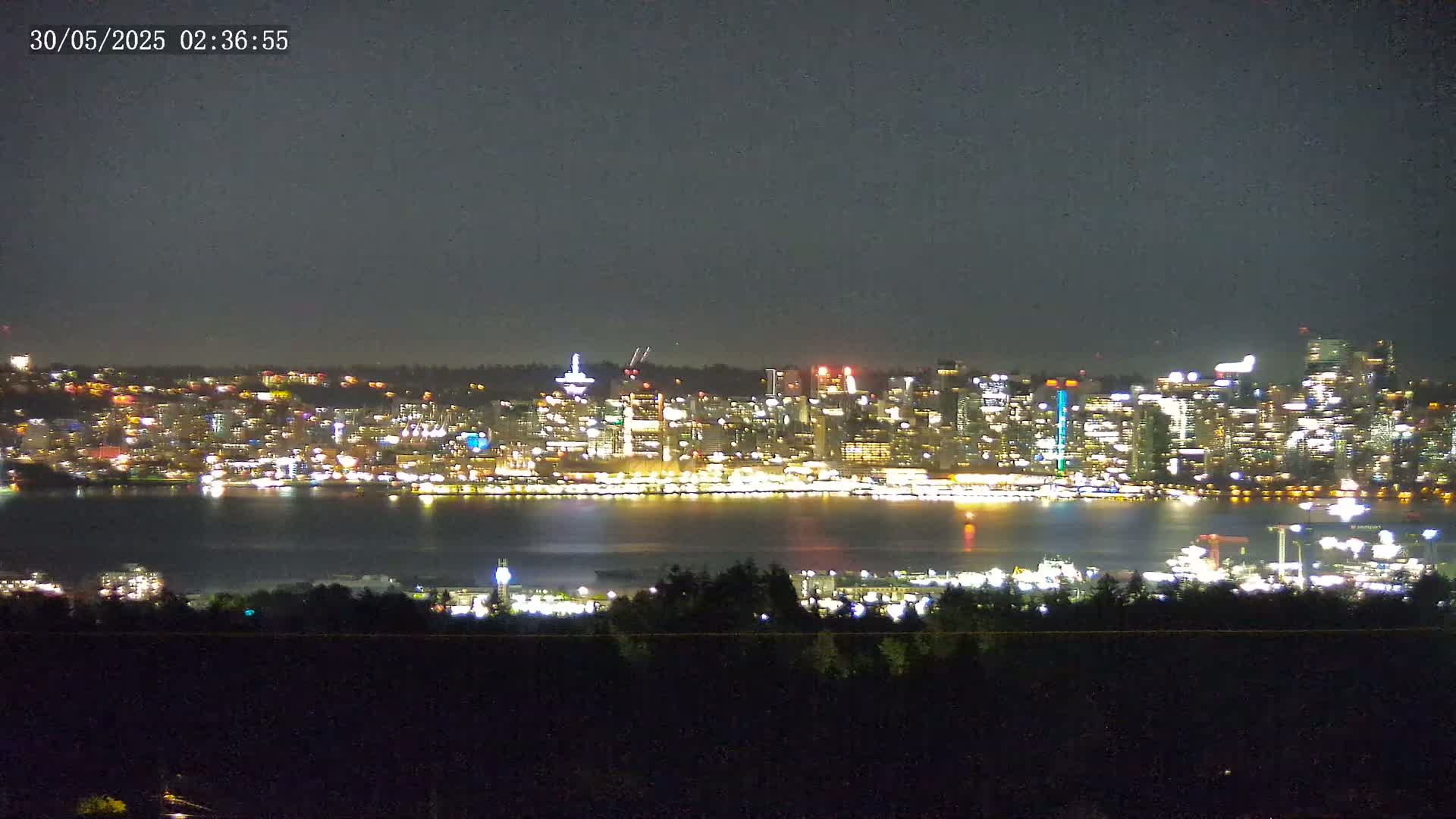 A brightly lit city skyline is visible across a dark body of water under a nighttime sky.
