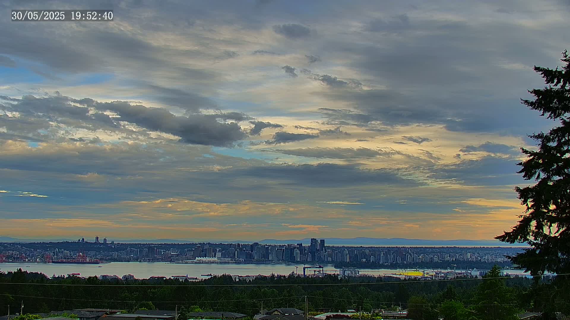 A city skyline is visible across a body of water under a partly cloudy sky with streaks of yellow and orange near the horizon.