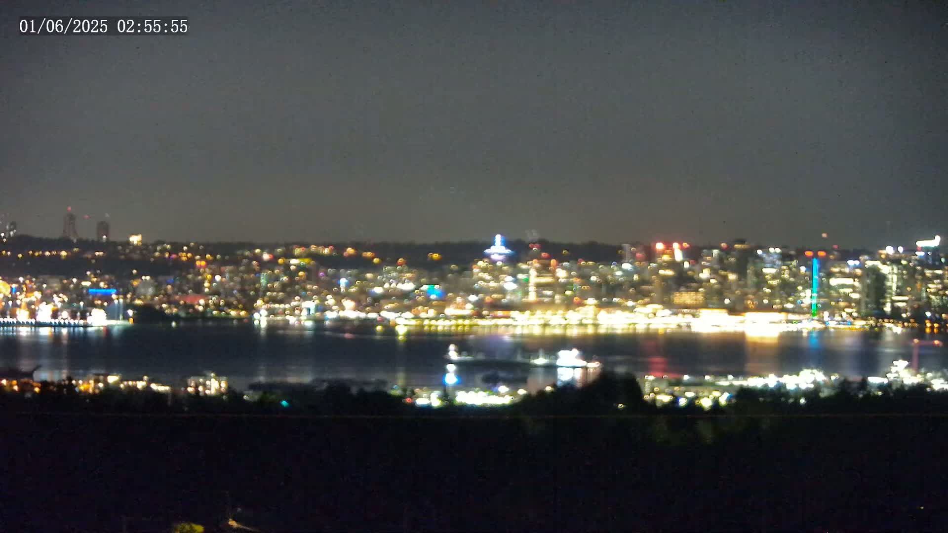 A nighttime view of a city skyline across a body of water, under a dark sky.
