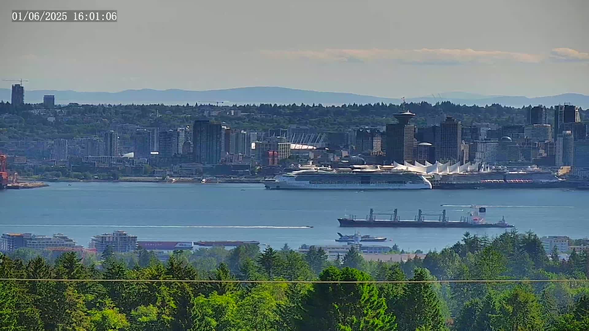 A large cruise ship and other vessels are in a harbor next to a city skyline on a partly cloudy day.