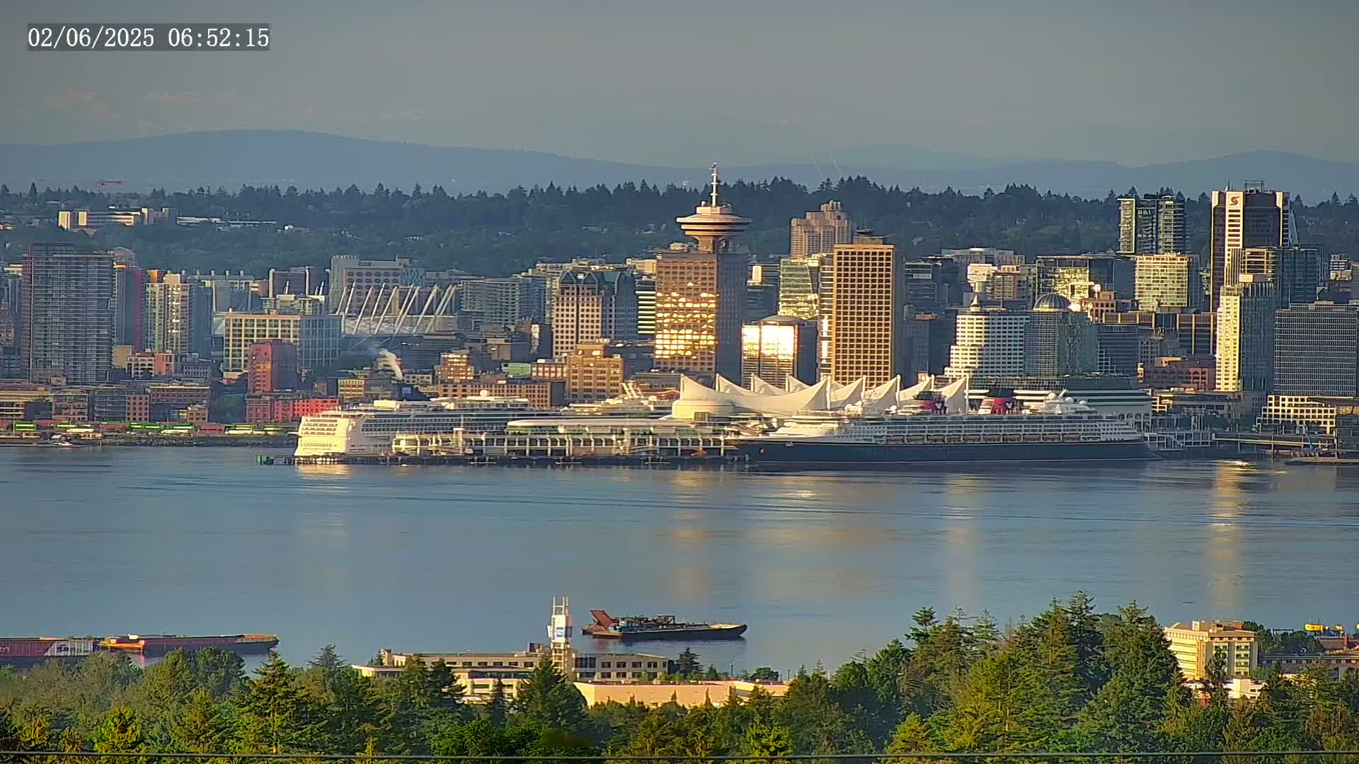 A large cruise ship is docked at a city harbor under a mostly clear sky, with mountains visible in the distance.