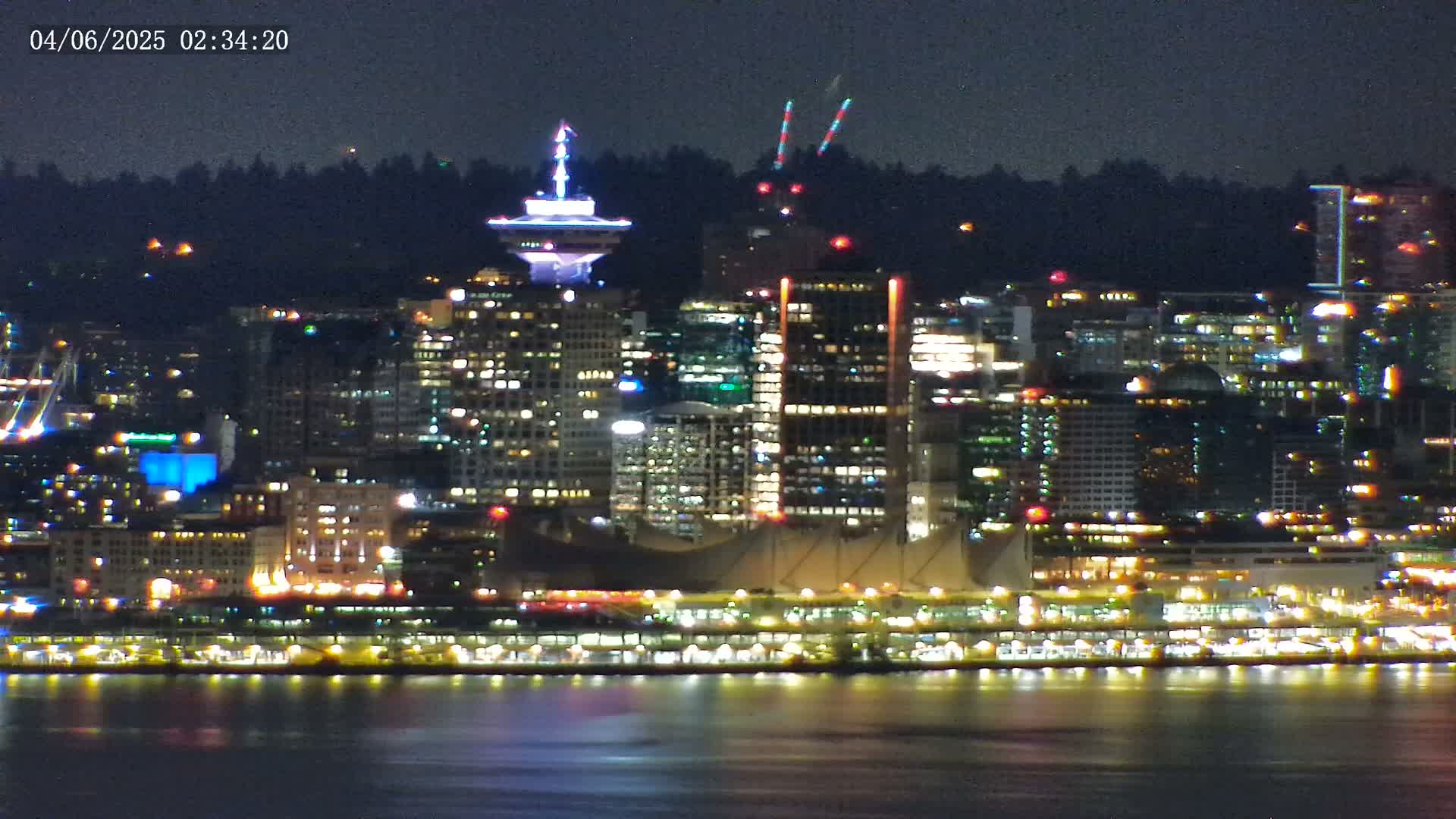 A brightly lit city skyline at night, viewed from across a body of dark water under a clear sky.