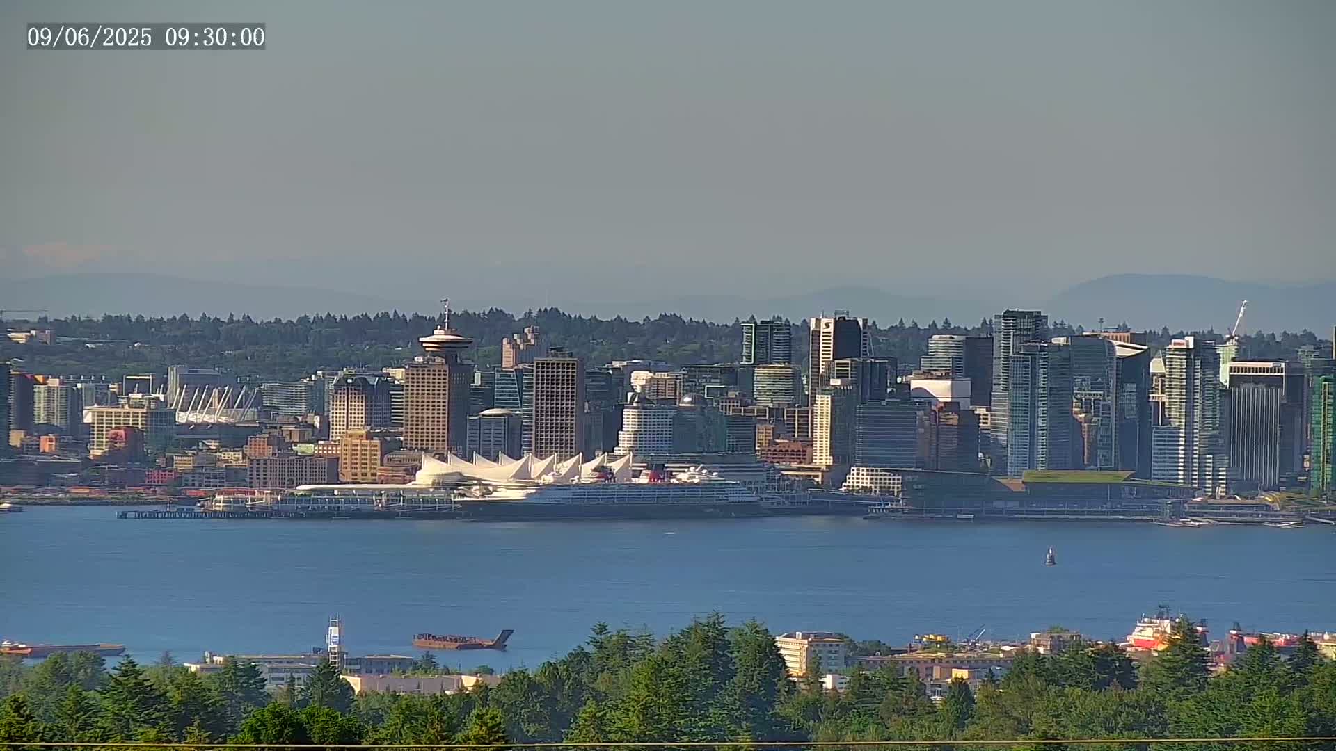 A distant view of a city skyline on a hazy day, featuring a large cruise ship docked at a waterfront terminal.