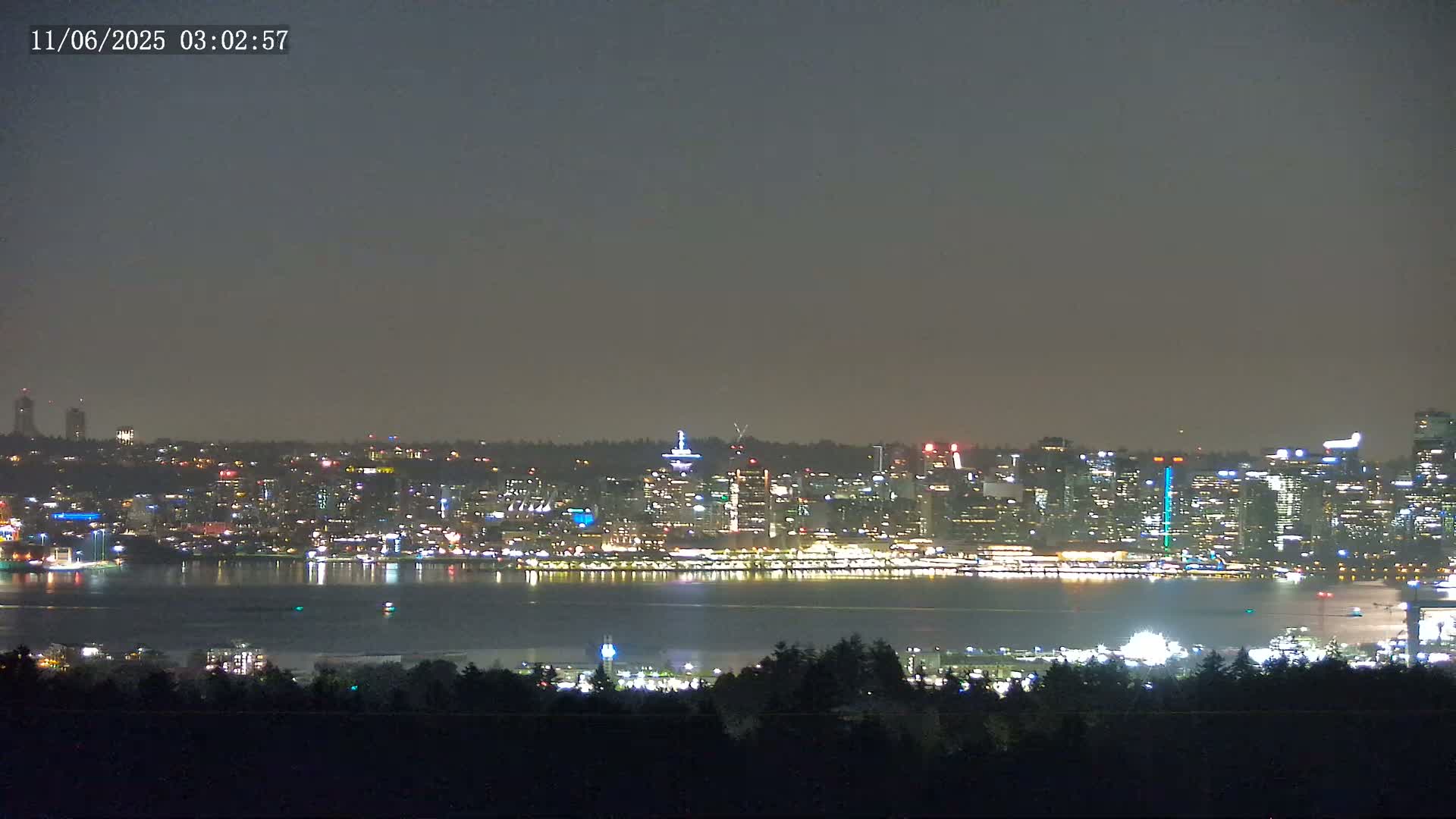 A nighttime view of a city skyline across a body of water, under a dark, hazy sky.