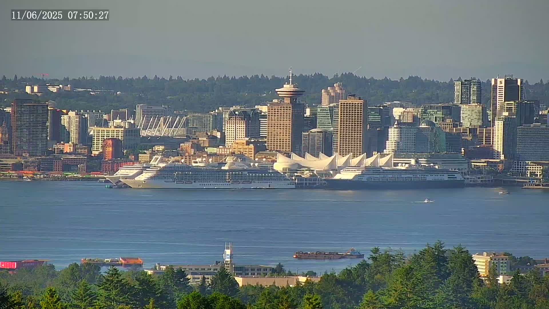 A hazy view shows a city skyline with several skyscrapers and a large cruise ship docked near a white sail-like structure, all situated on a calm body of water.