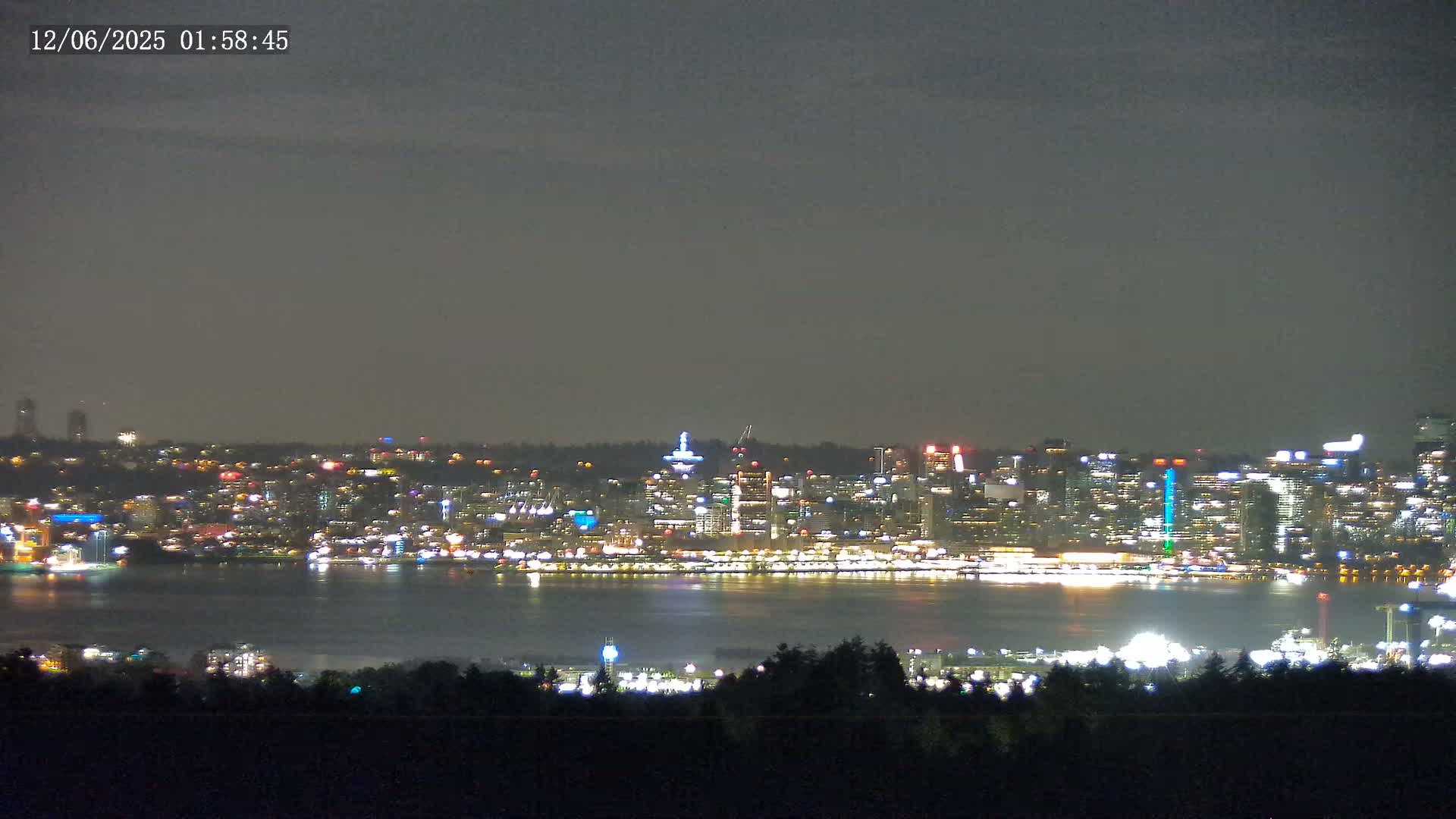A nighttime view of a city skyline across a body of water, under a dark, cloudy sky.