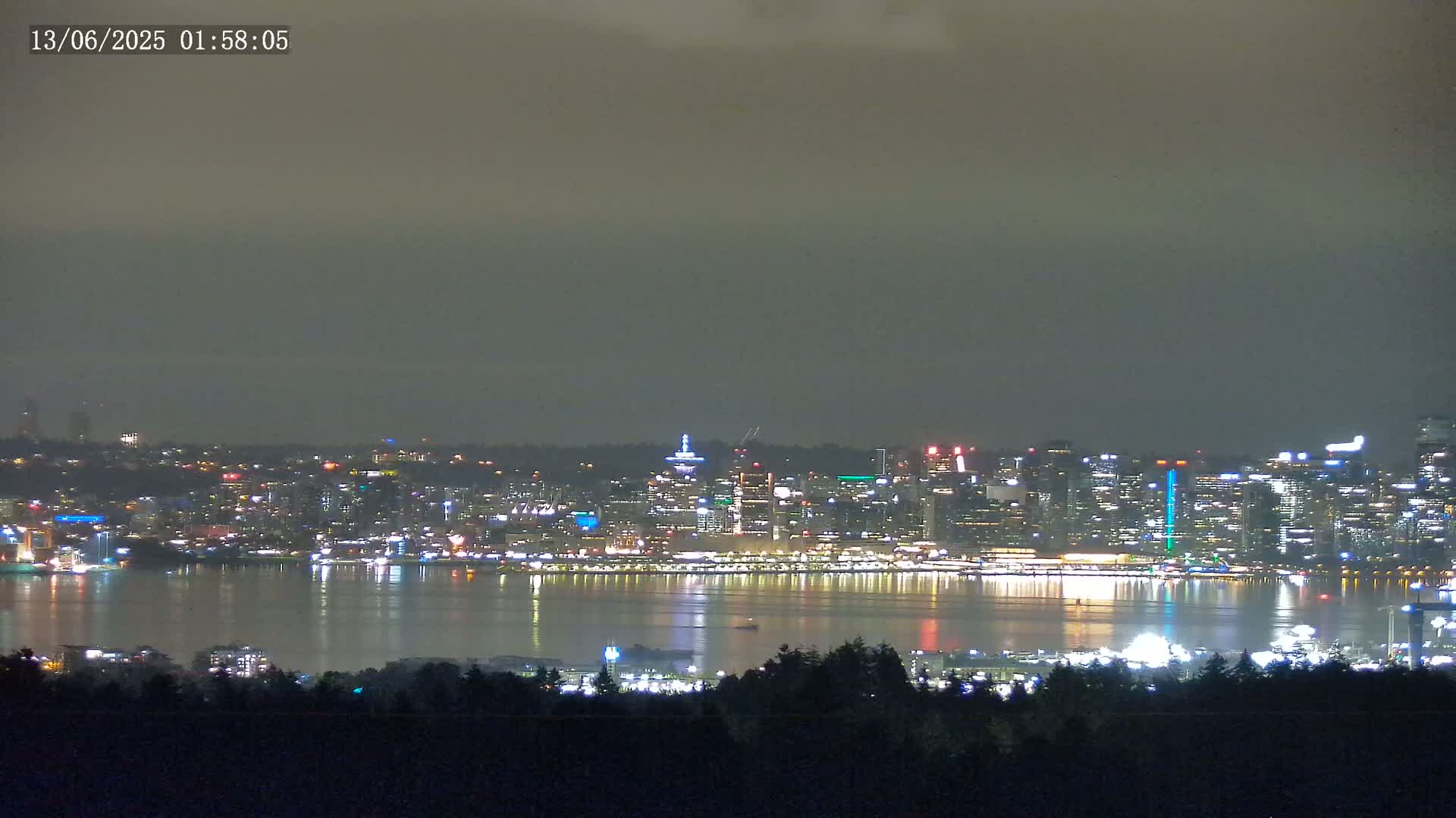 A nighttime view of a city skyline across a body of water under an overcast sky.