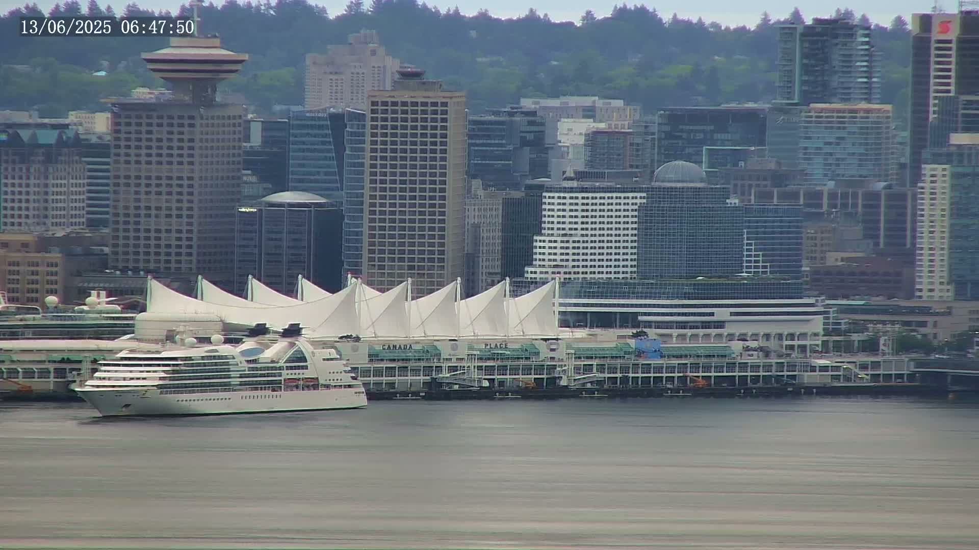 A cruise ship is docked at a waterfront terminal in a city with many high-rise buildings on a hazy day.