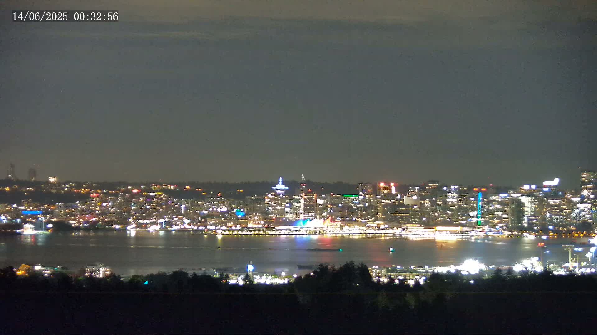 A brightly lit city skyline is visible across a dark body of water under a mostly clear night sky.