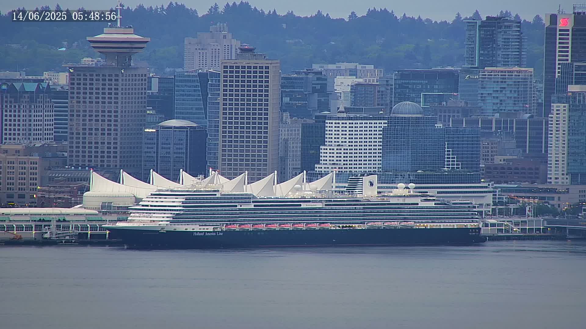 A large cruise ship is docked at a waterfront terminal in a city with many high-rise buildings, under an overcast sky.