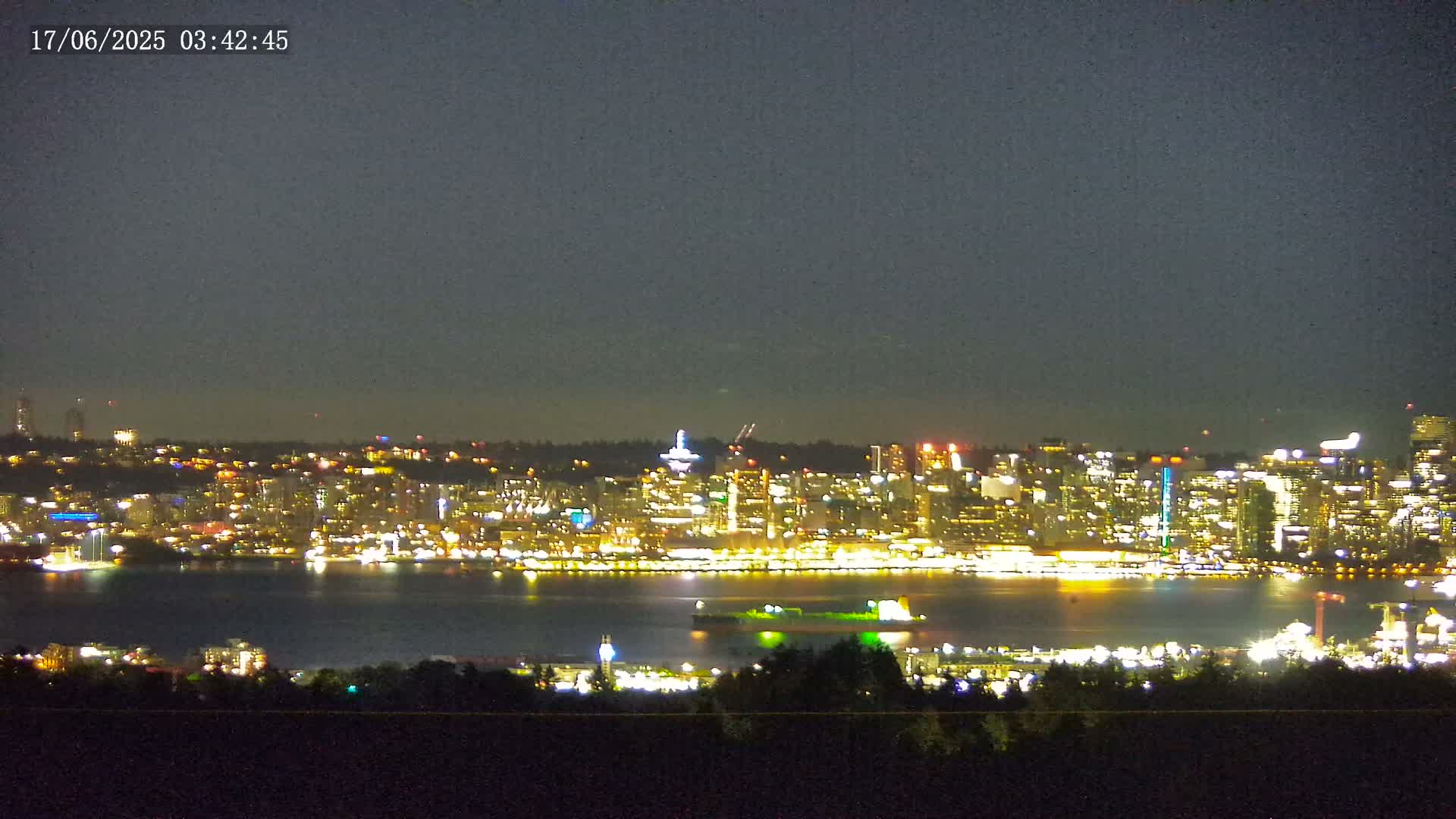 A brightly lit city skyline across a dark body of water is visible at night under a mostly clear sky.