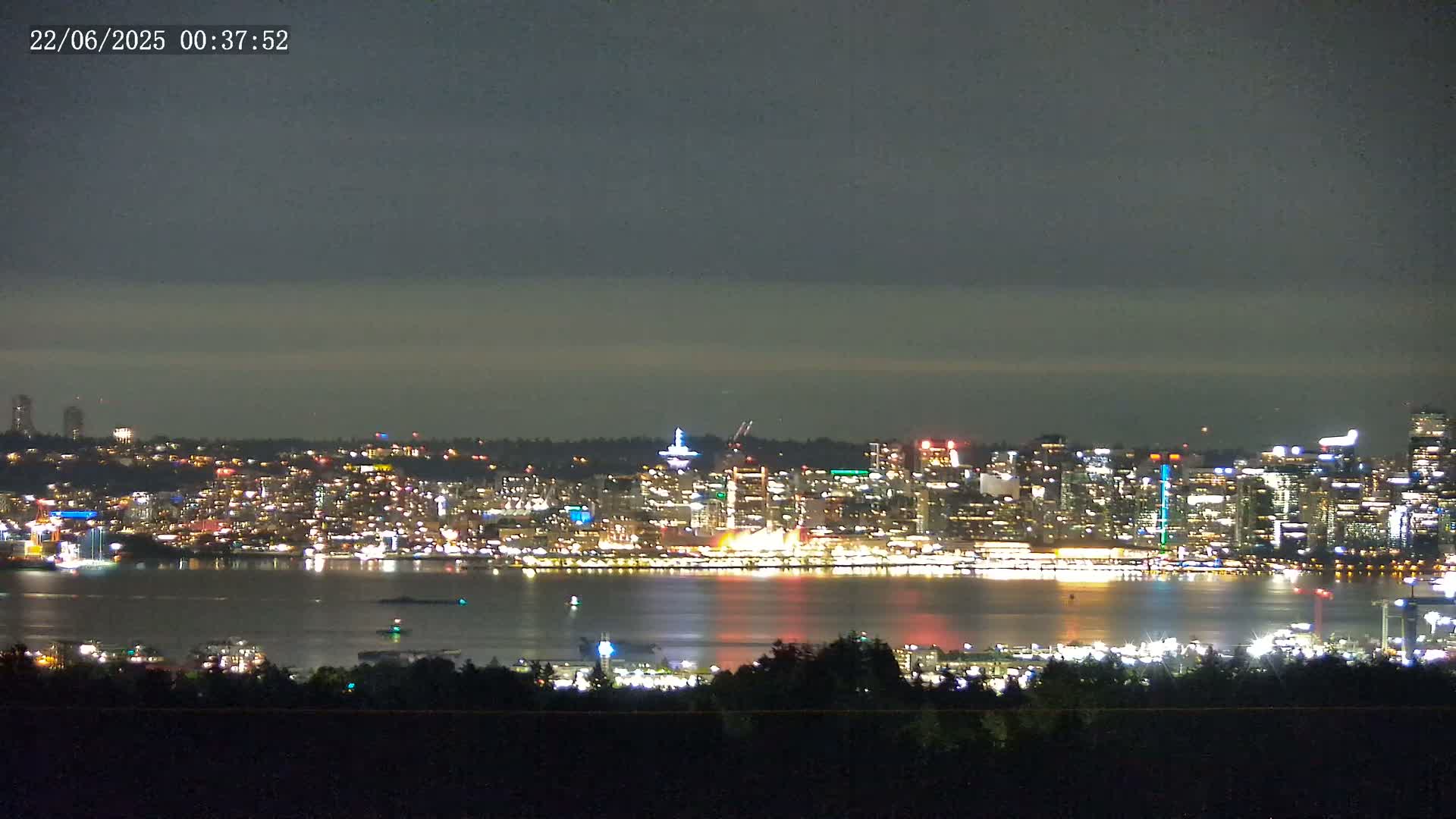 A nighttime view of a city skyline across a body of water under a mostly cloudy sky.