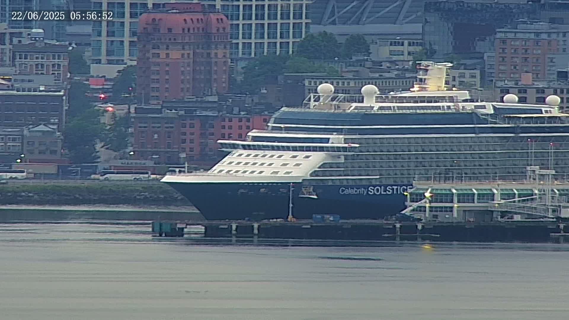 A large cruise ship is docked at a pier next to a city under an overcast sky.
