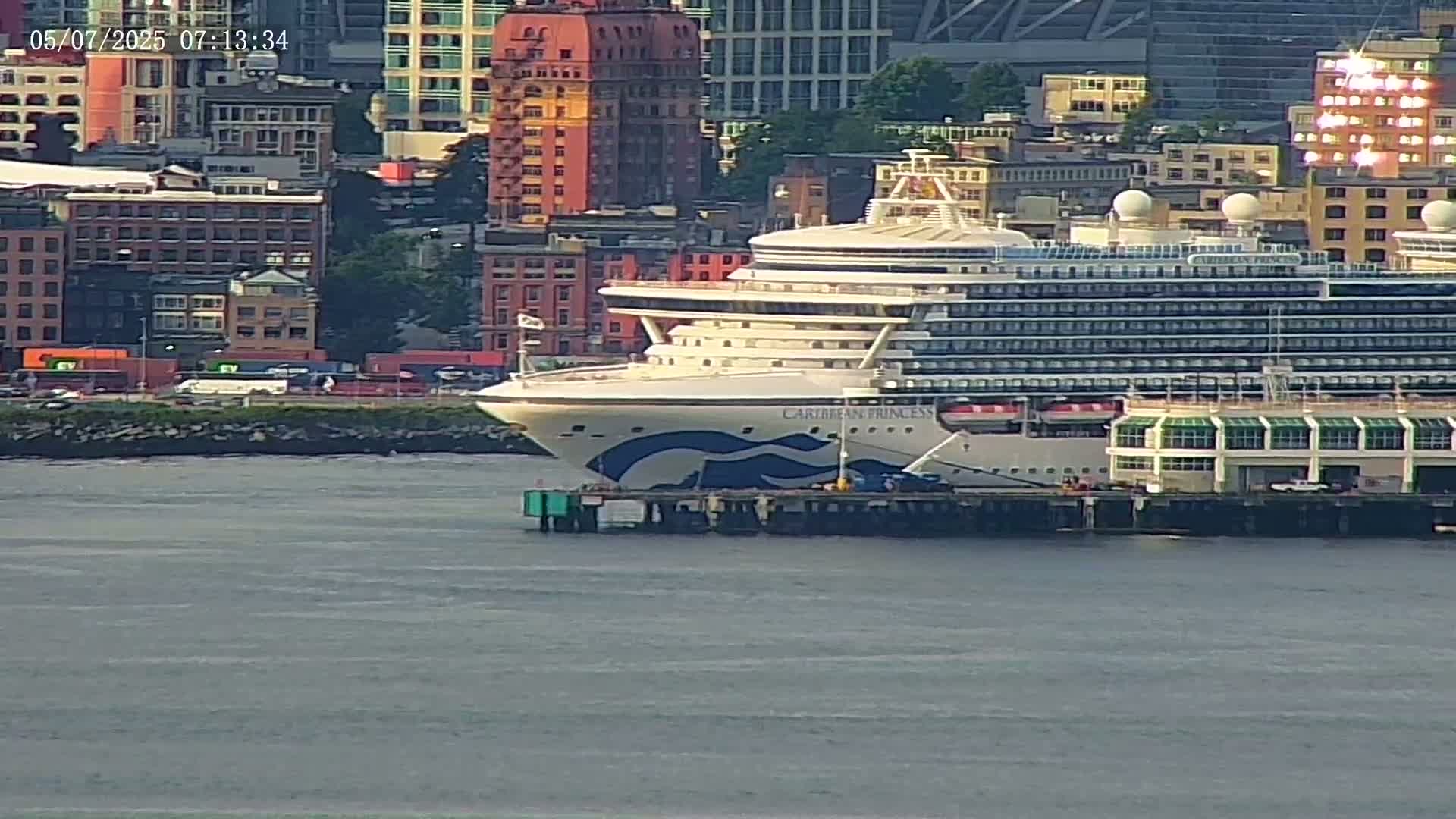 A large cruise ship is docked at a pier next to a city skyline on a calm day.