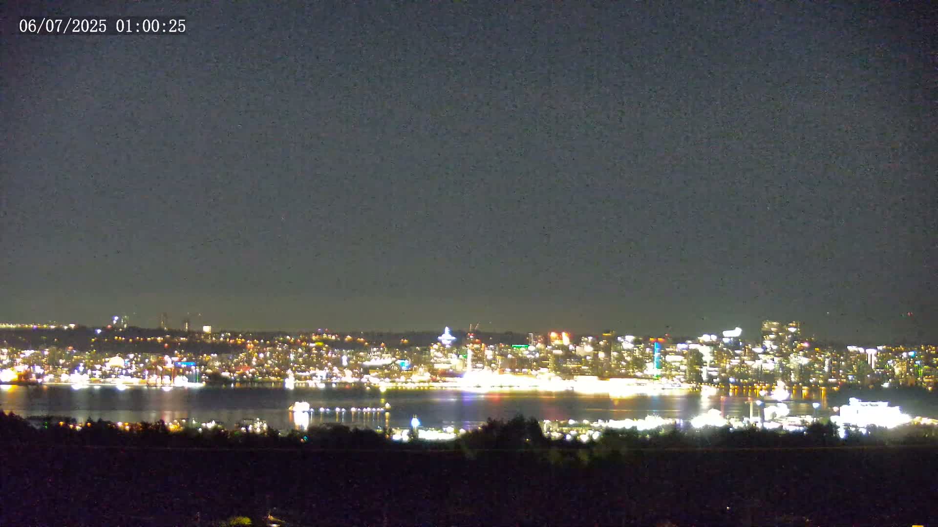A nighttime long shot shows a city skyline across a body of water, under a clear, dark sky.
