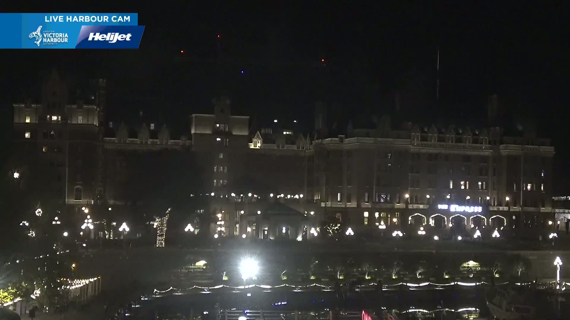 At night, a large, illuminated building stands, with decorative lights outlining its base and a few distant lights in the sky.
